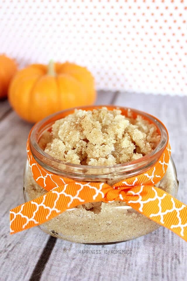 A glass jar of vanilla pumpkin spice sugar scrub with an orange bow on a wood background with a mini pumpkin