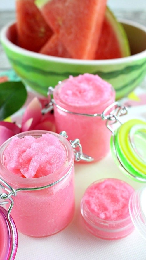 Two glass jars of pink watermelon lip scrub with watermelon in background