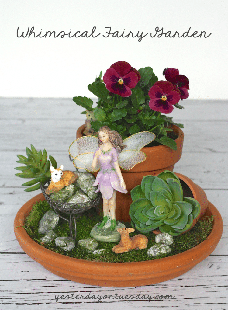Red flowers in terra cotta pot with fairy figurine in front and greenery with small animal figurines