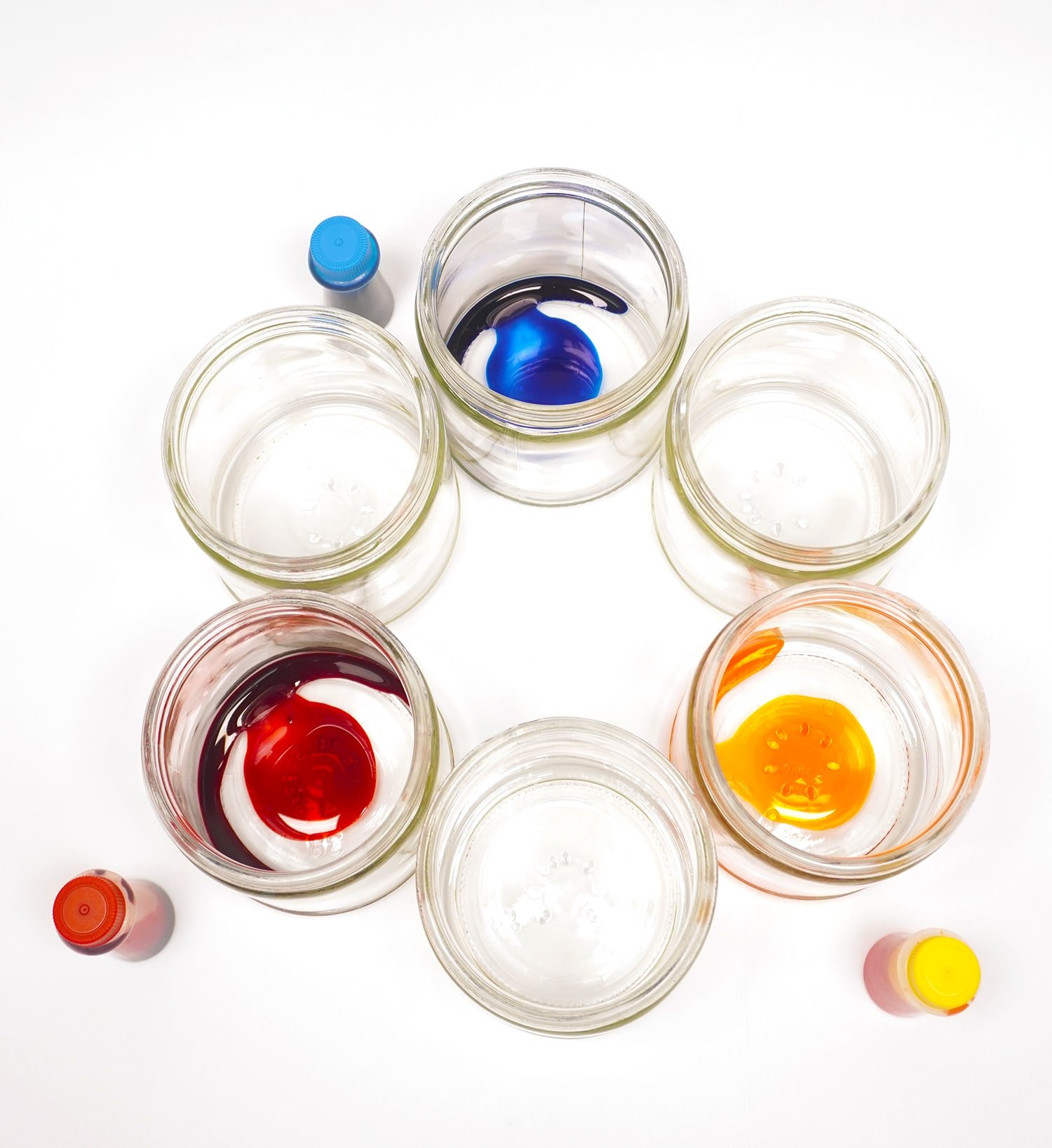 drops of red, yellow, and blue food coloring in 3 out of 6 jars placed in a circle 
