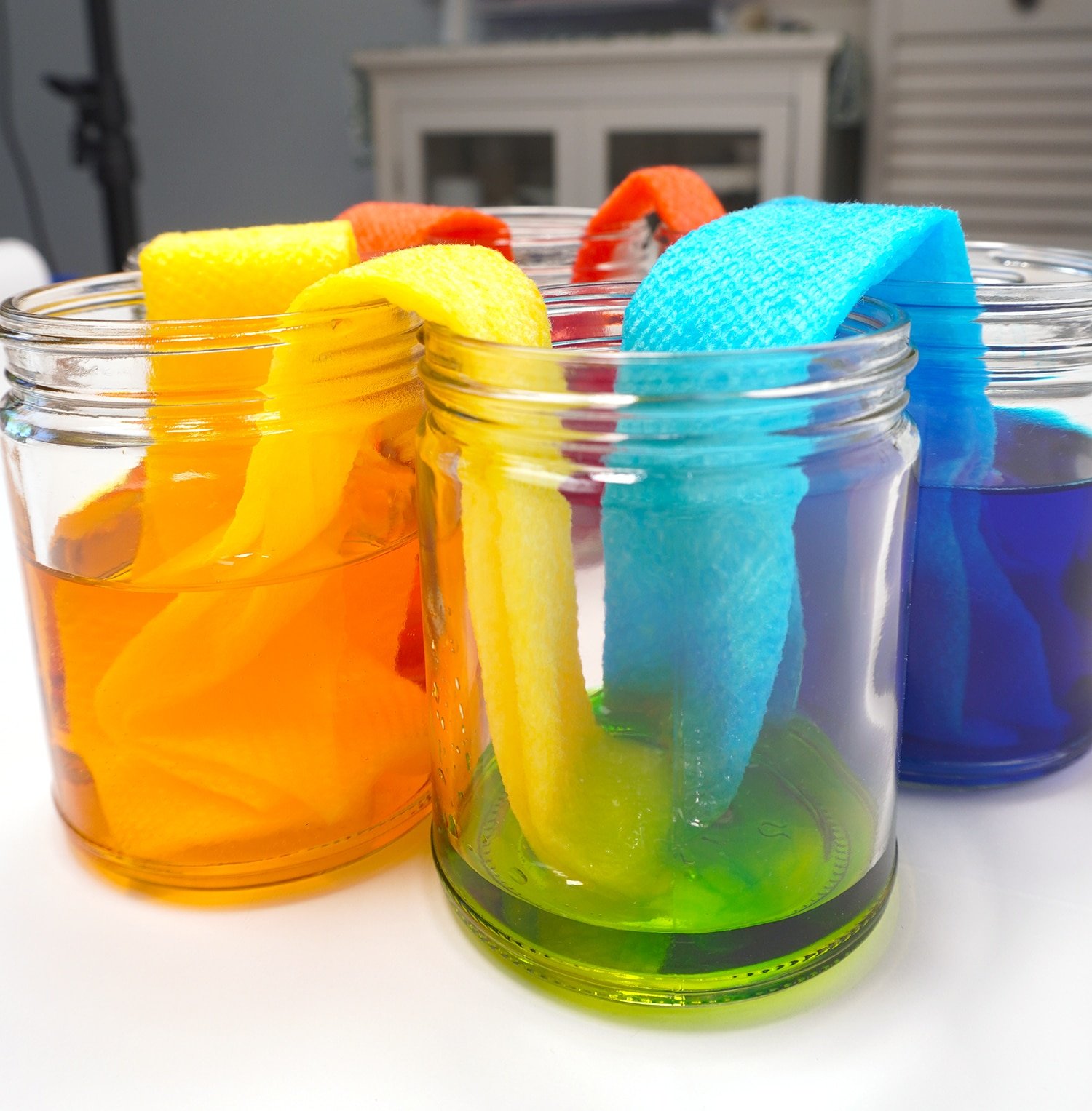 empty jars now filling with the secondary colors from submerged paper strips in primary color jars