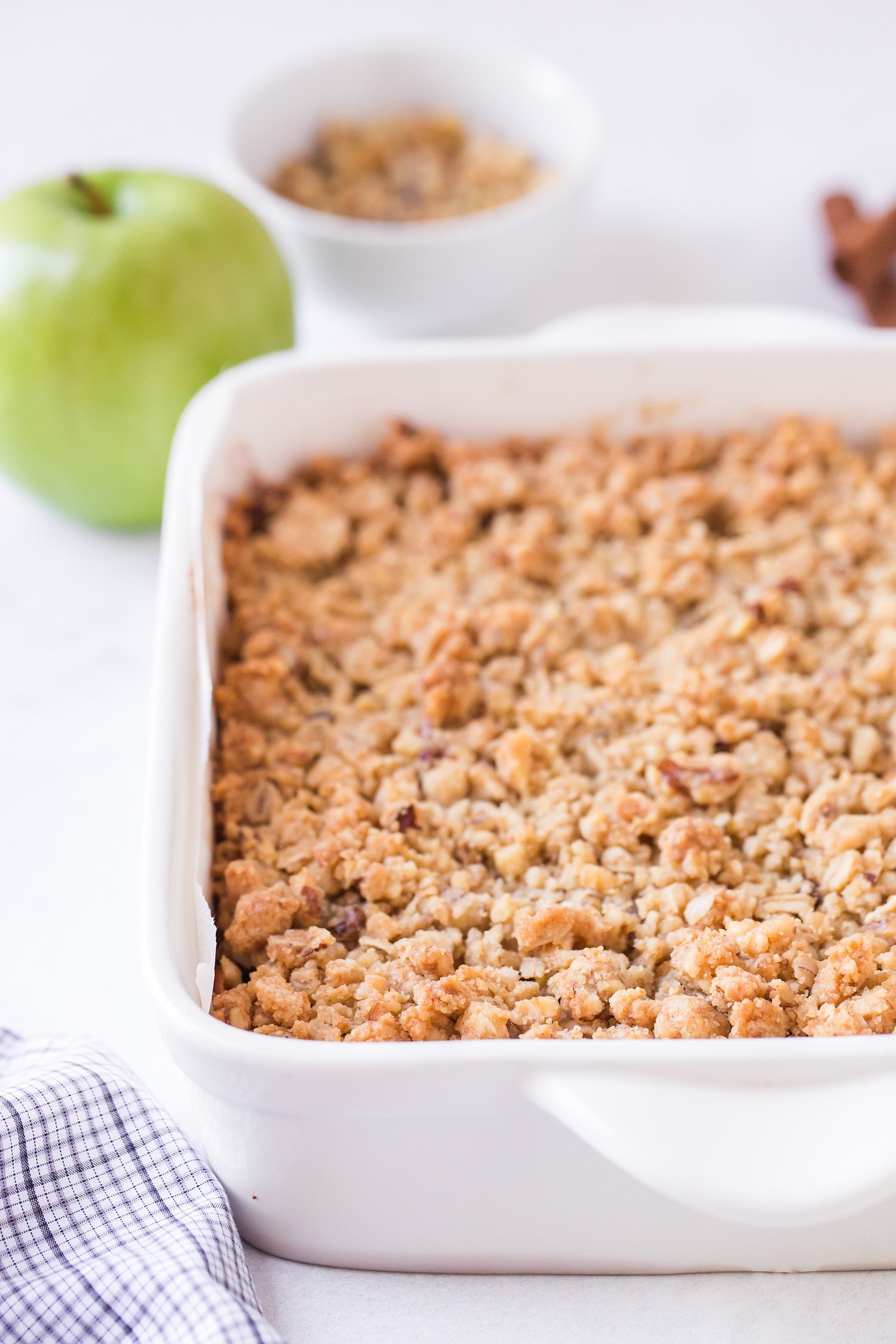 Apple pie bars in white baking dish with green apples in background