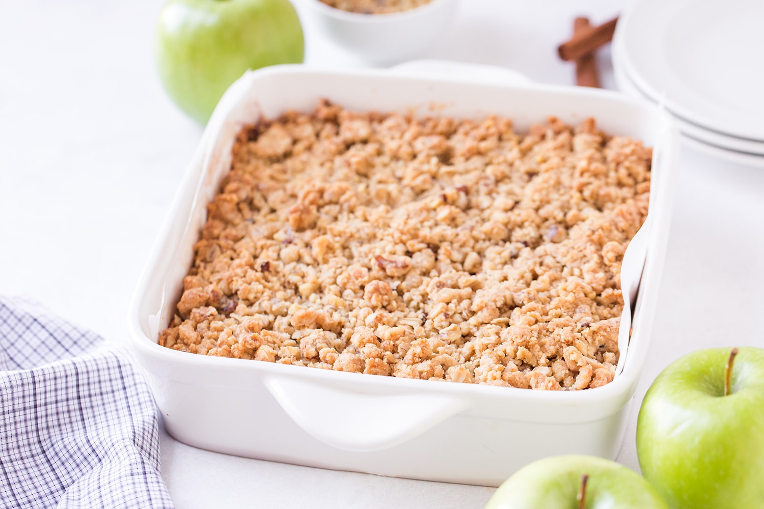 White baking dish with apple pie bars and streusel topping with apples on the side