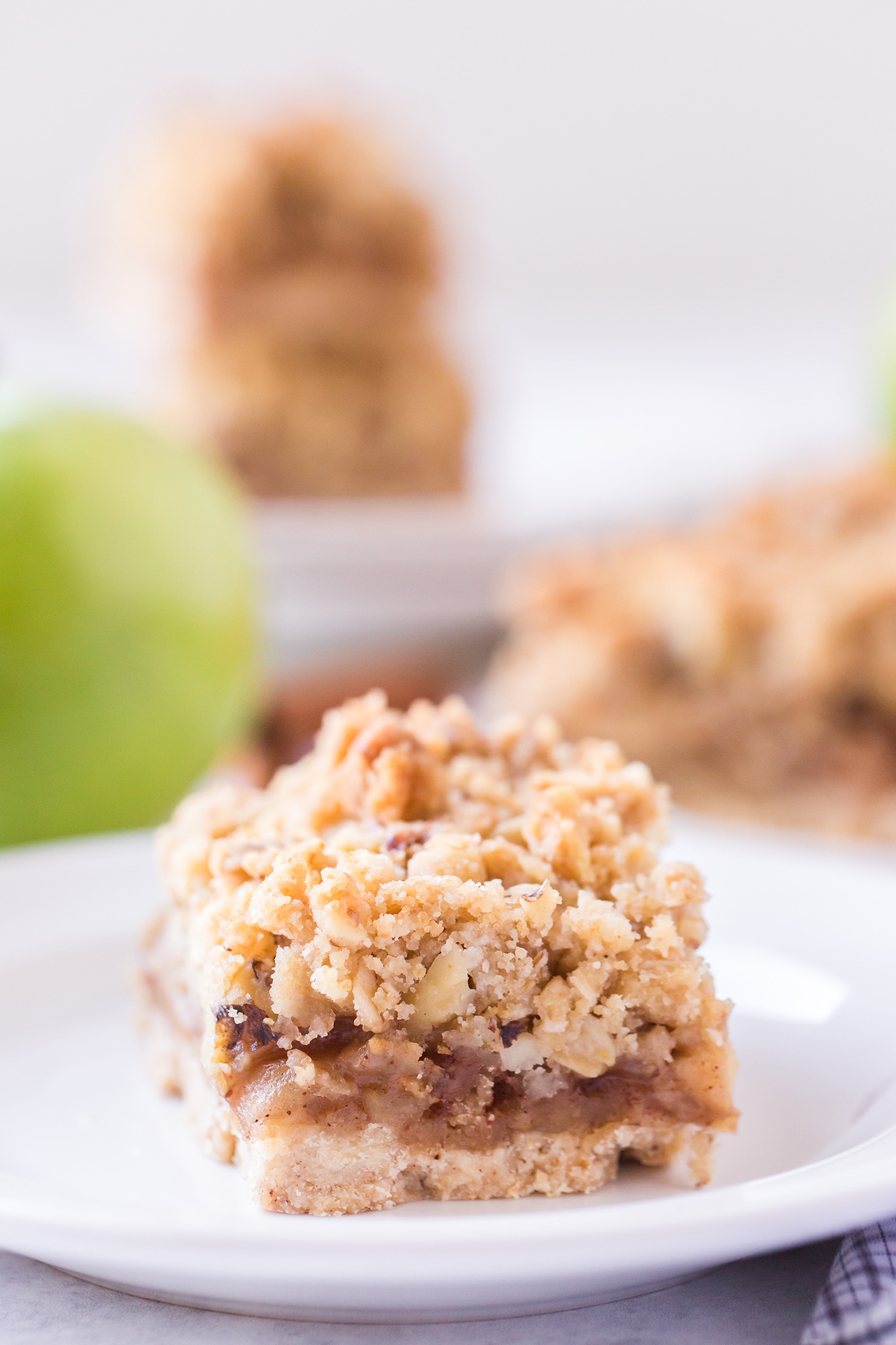 Apple pie bar on white plate with apples and more bars in the background