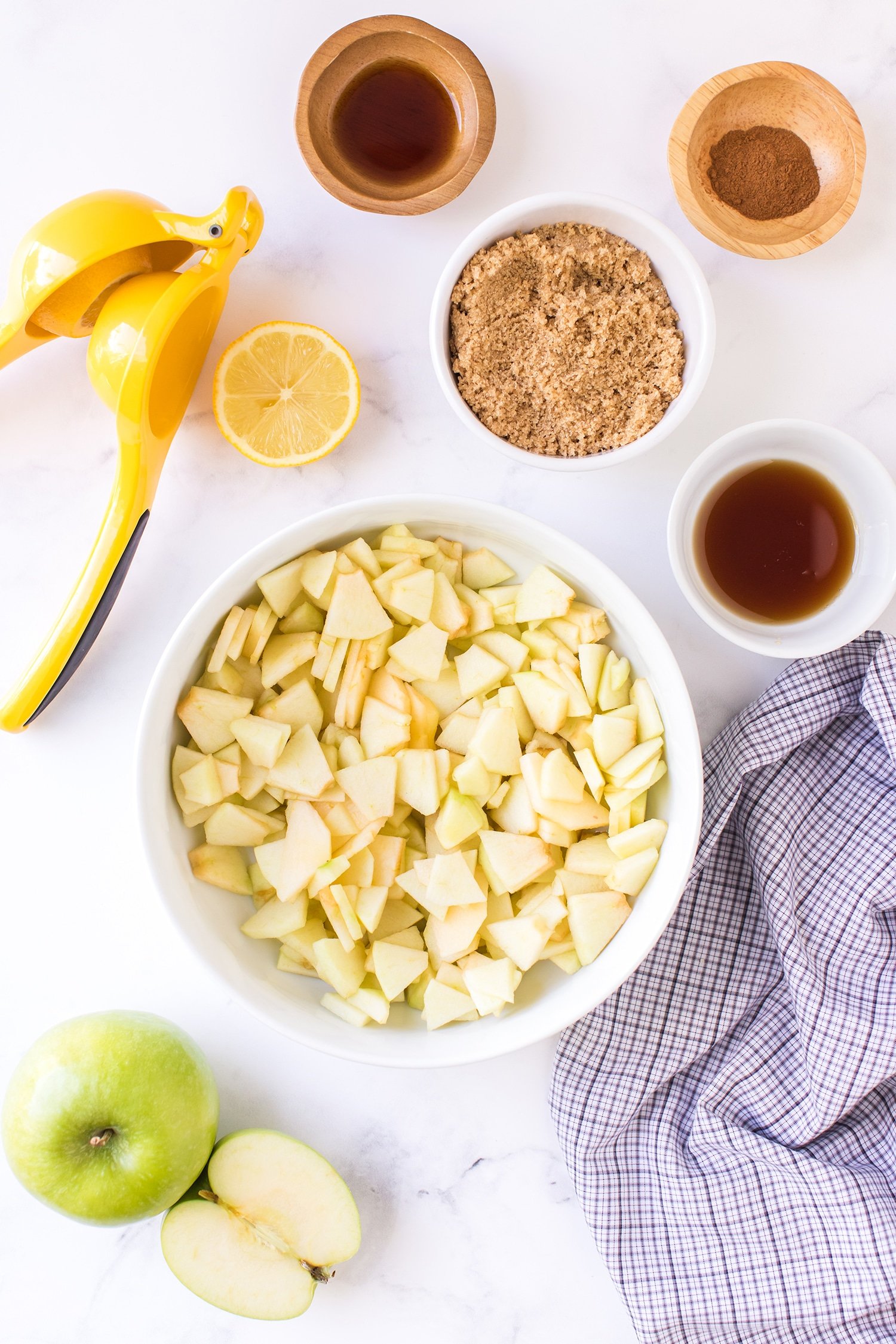 Sliced apples in mixing bowl surrounded by bowls of brown sugar and spices