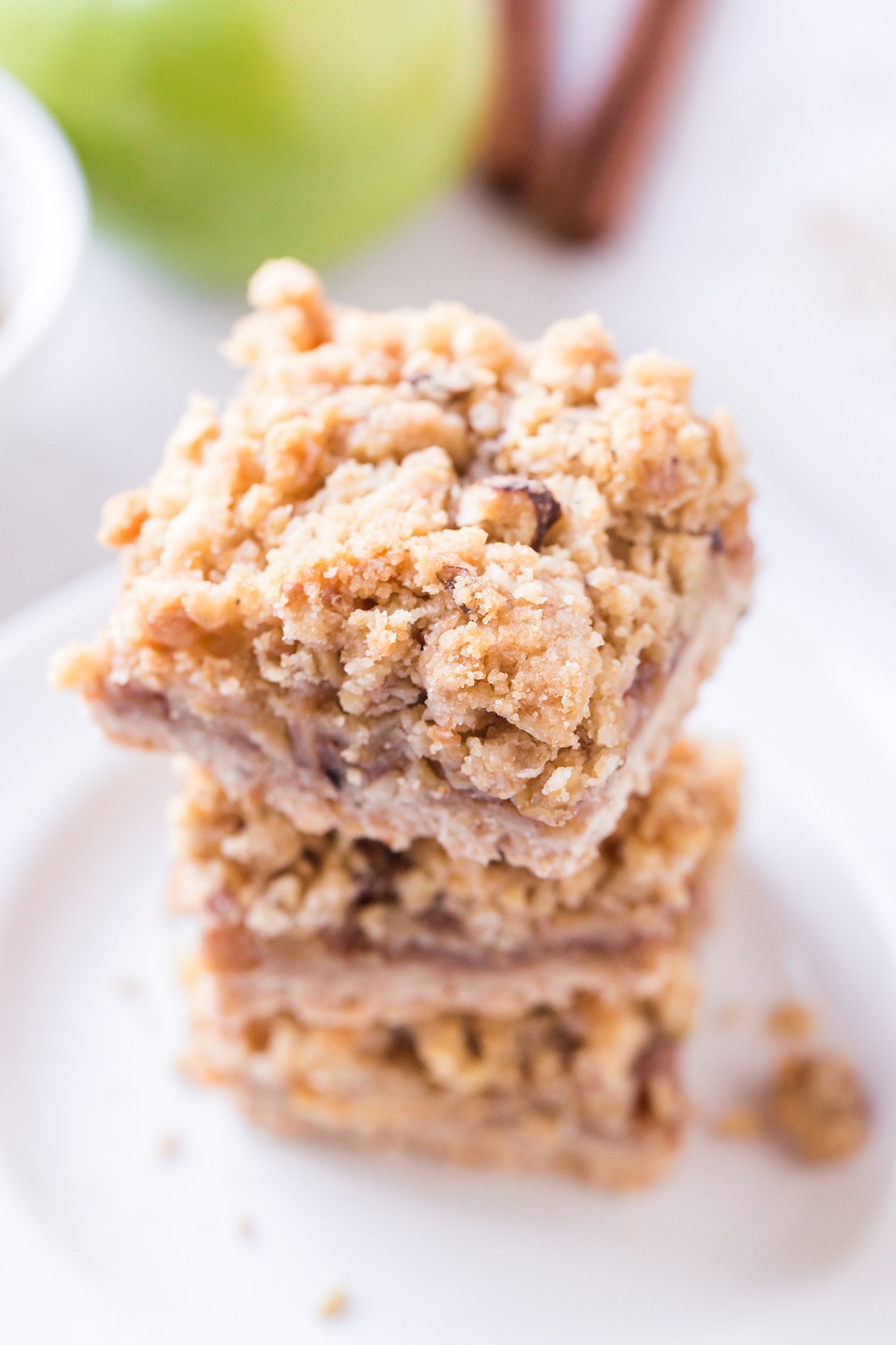 Three Apple Pie Bars stacked on a white plate with green apples in the background