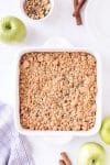 Apple pie bars with streusel topping in white backing dish with green apple on the side