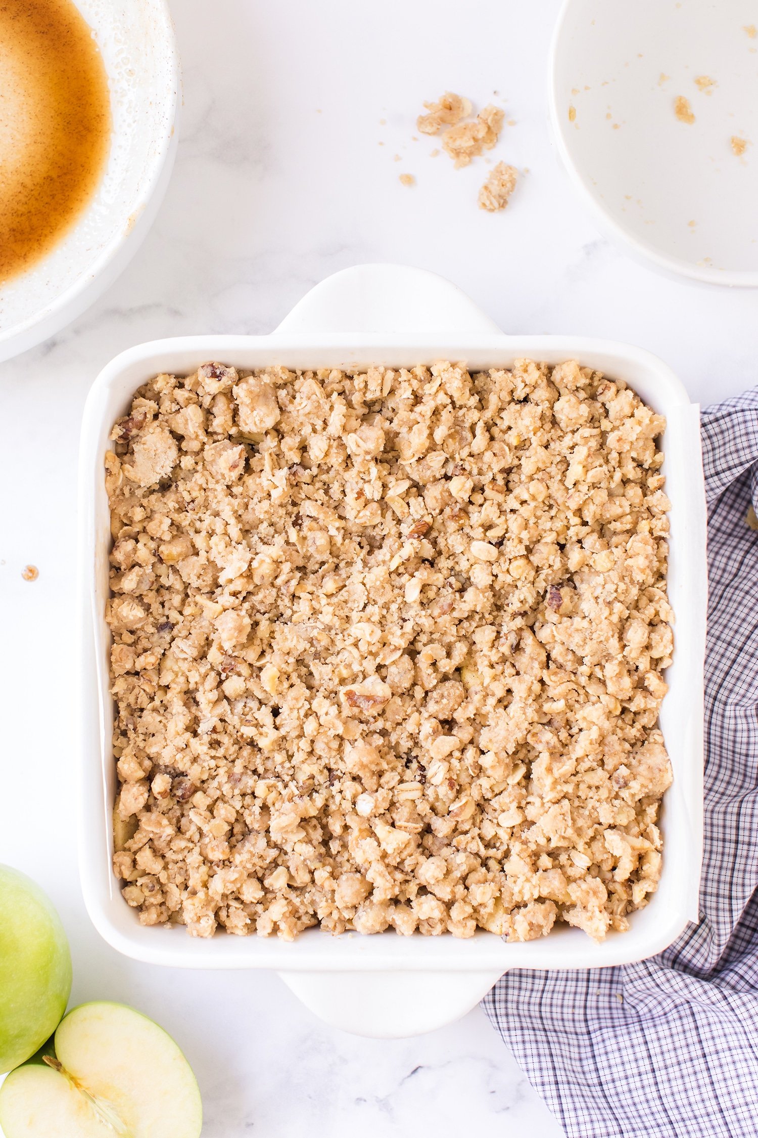 Closeup of apple pie bars with streusel topping in white backing dish with green apple on the side