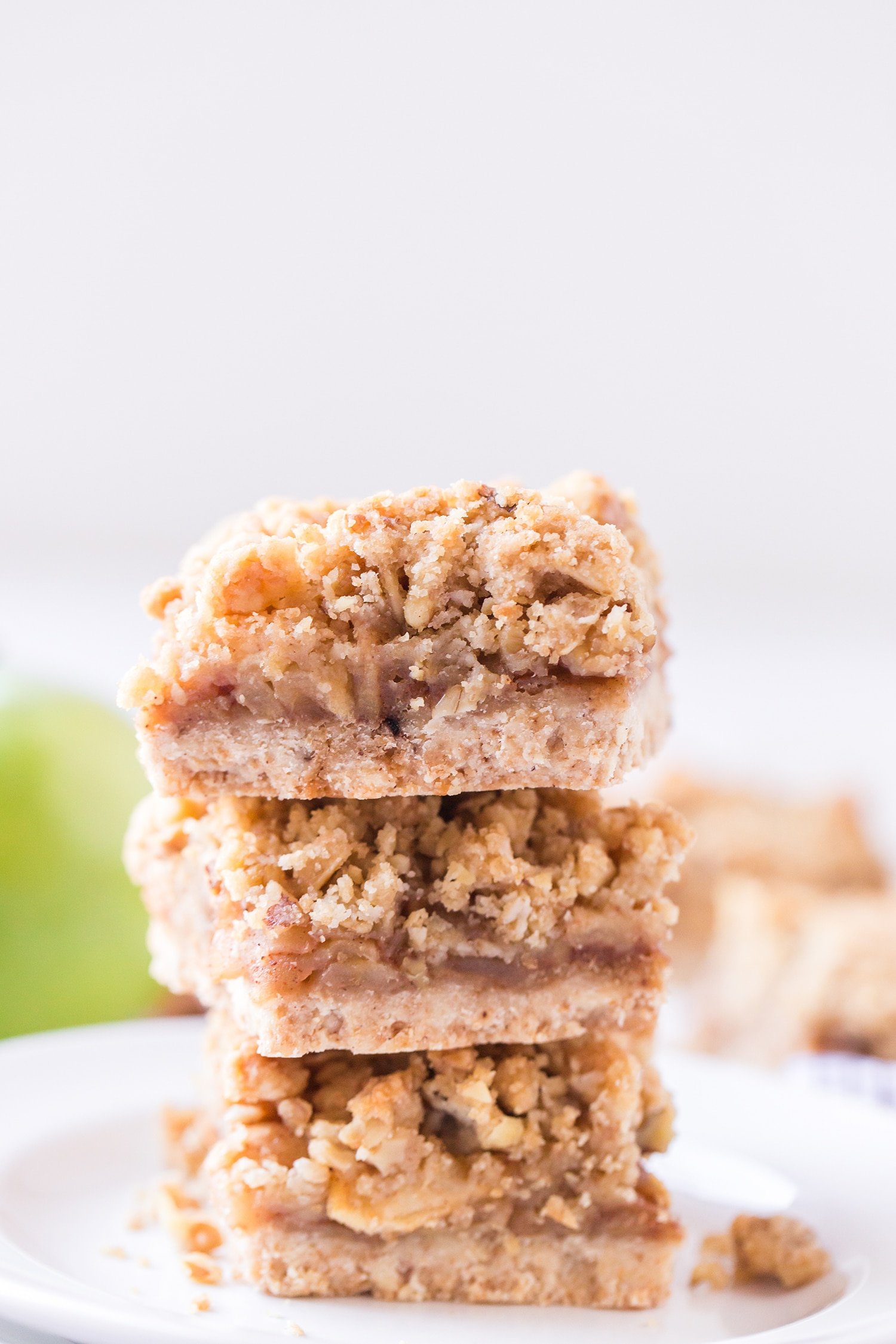 Three Apple Pie Bars stacked on a white plate with green apples in the background
