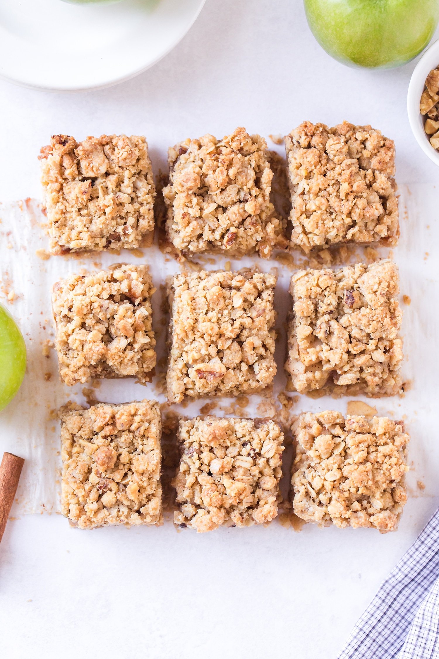 Sliced apple pie bars on white marble background surrounded by green apples and cinnamon sticks