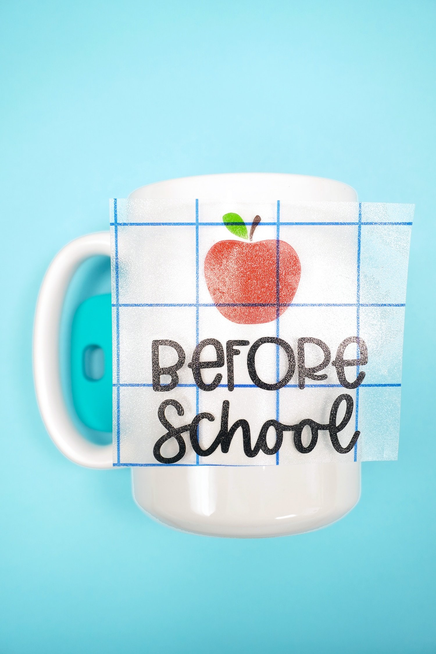 "Before School" and apple vinyl designs on transfer tape in the process of being applied to a white mug