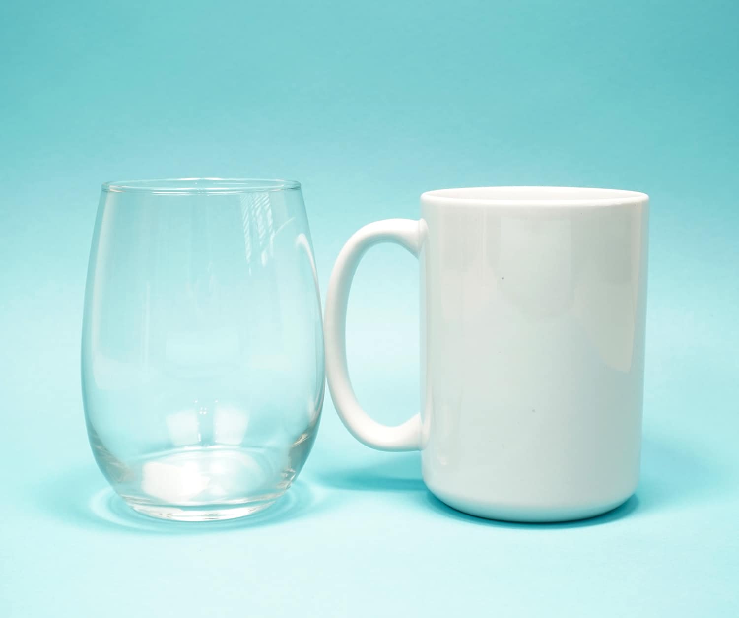 Clear stemless wine glass and white mug on light blue background