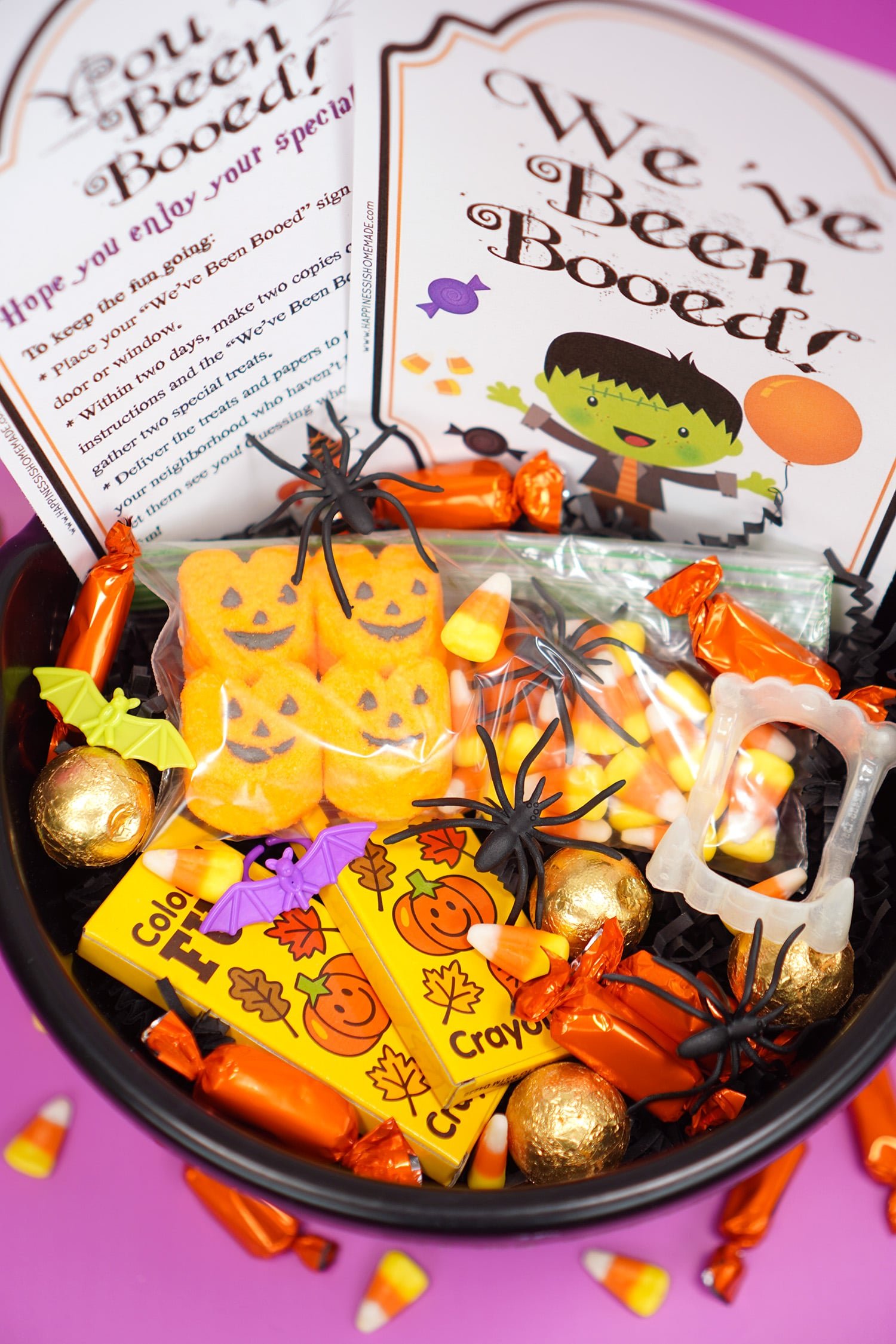 Booed printables and Boo Basket filled with Hallowen candy and novelty toys with \"You\'ve Been Booed\"and \" We\'ve Been Booed\" printable signs on purple background