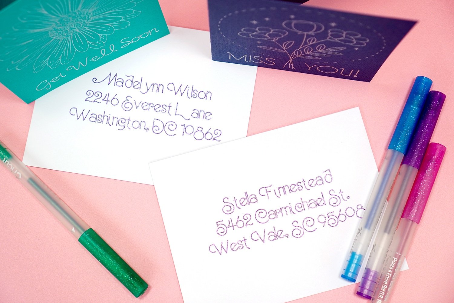 Glitter addressed white envelopes on pink background with glitter pens and cards