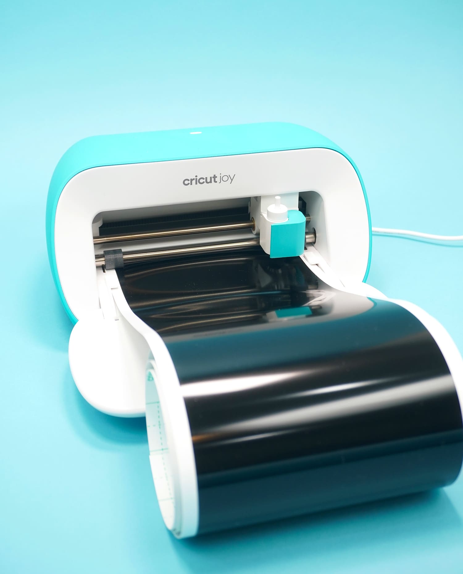 Cricut Joy machine loaded with black Smart Vinyl on blue background