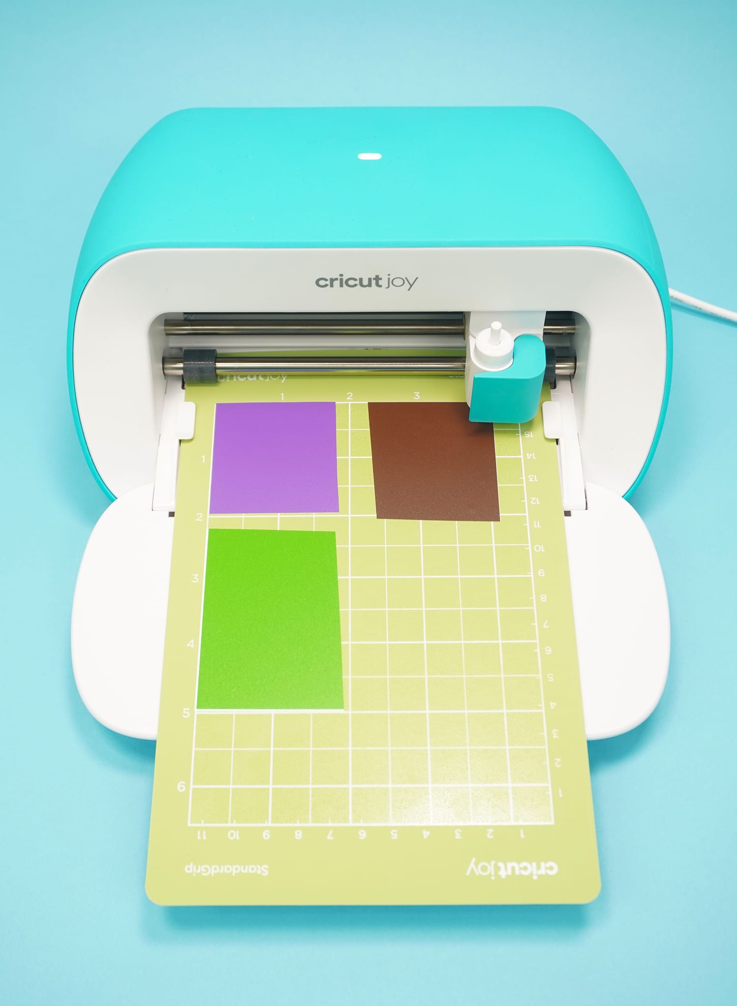 Cricut Joy machine with green cutting mat and scraps of purple, brown, and green vinyl