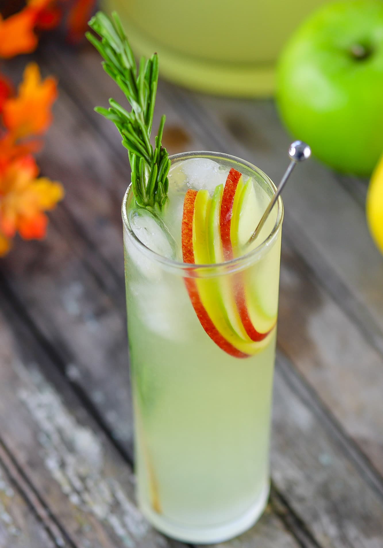 Hard lemonade in glass garnished with apple slices and a sprig of rosemary