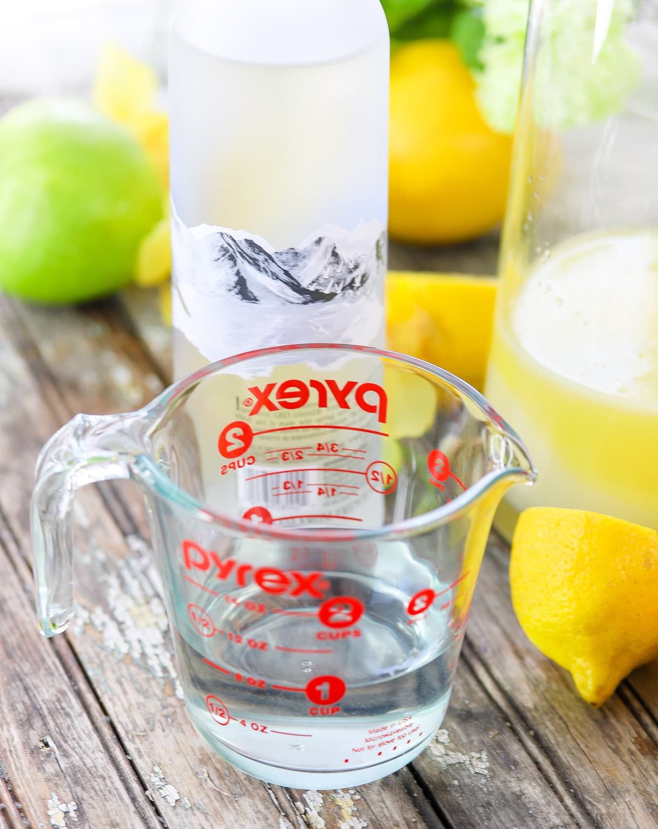 apple flavored vodka in a measuring cup with vodka bottle, lemons, and apples in background