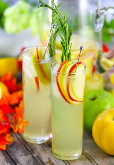 Two tall glasses of hard lemonade garnished with apple slices and a sprig of rosemary