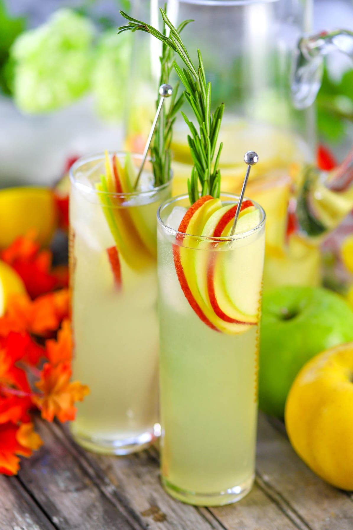 Two tall glasses of hard lemonade garnished with apple slices and a sprig of rosemary