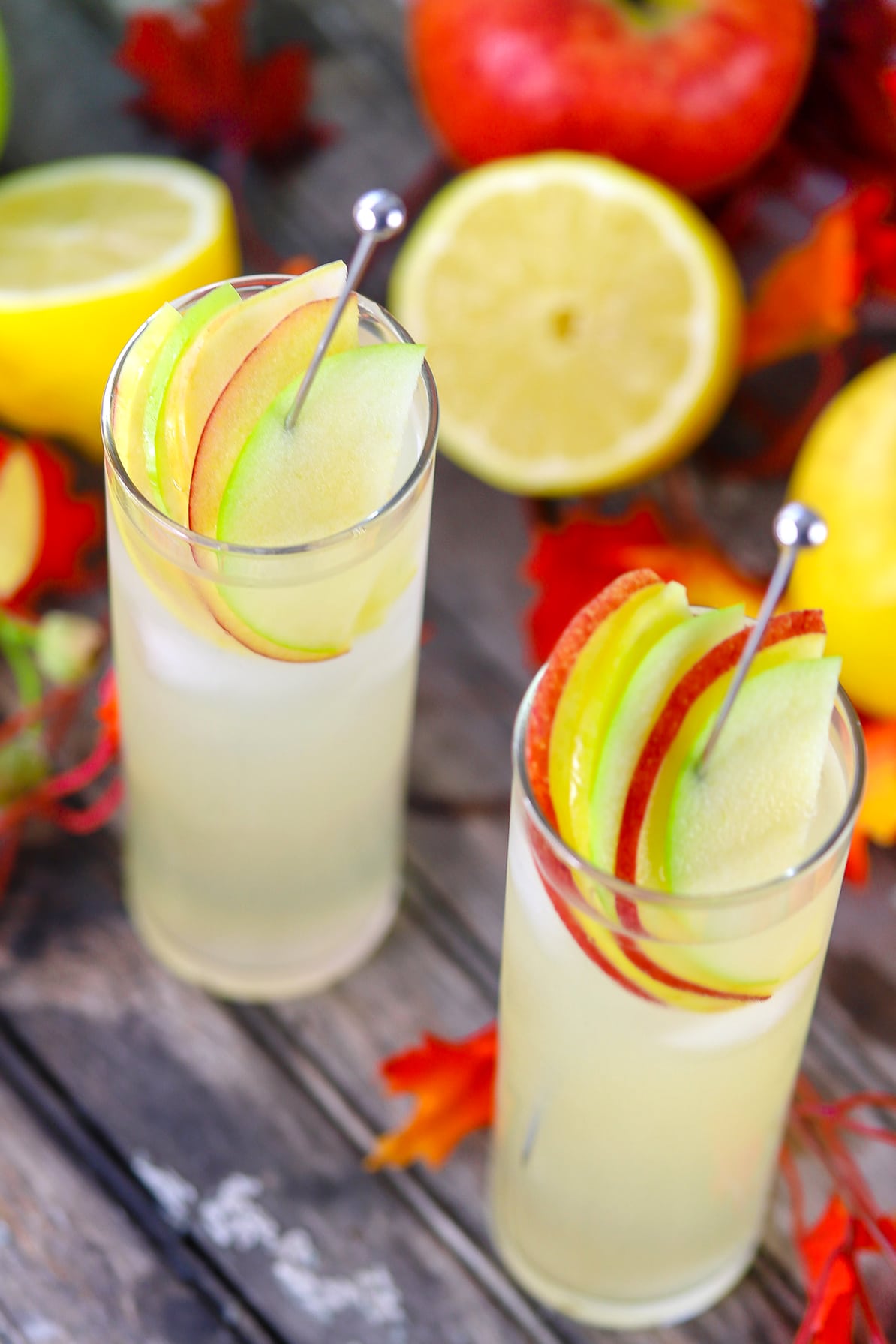 Hard lemonade in glass garnished with apple slices on a stainless steel drink stirrer