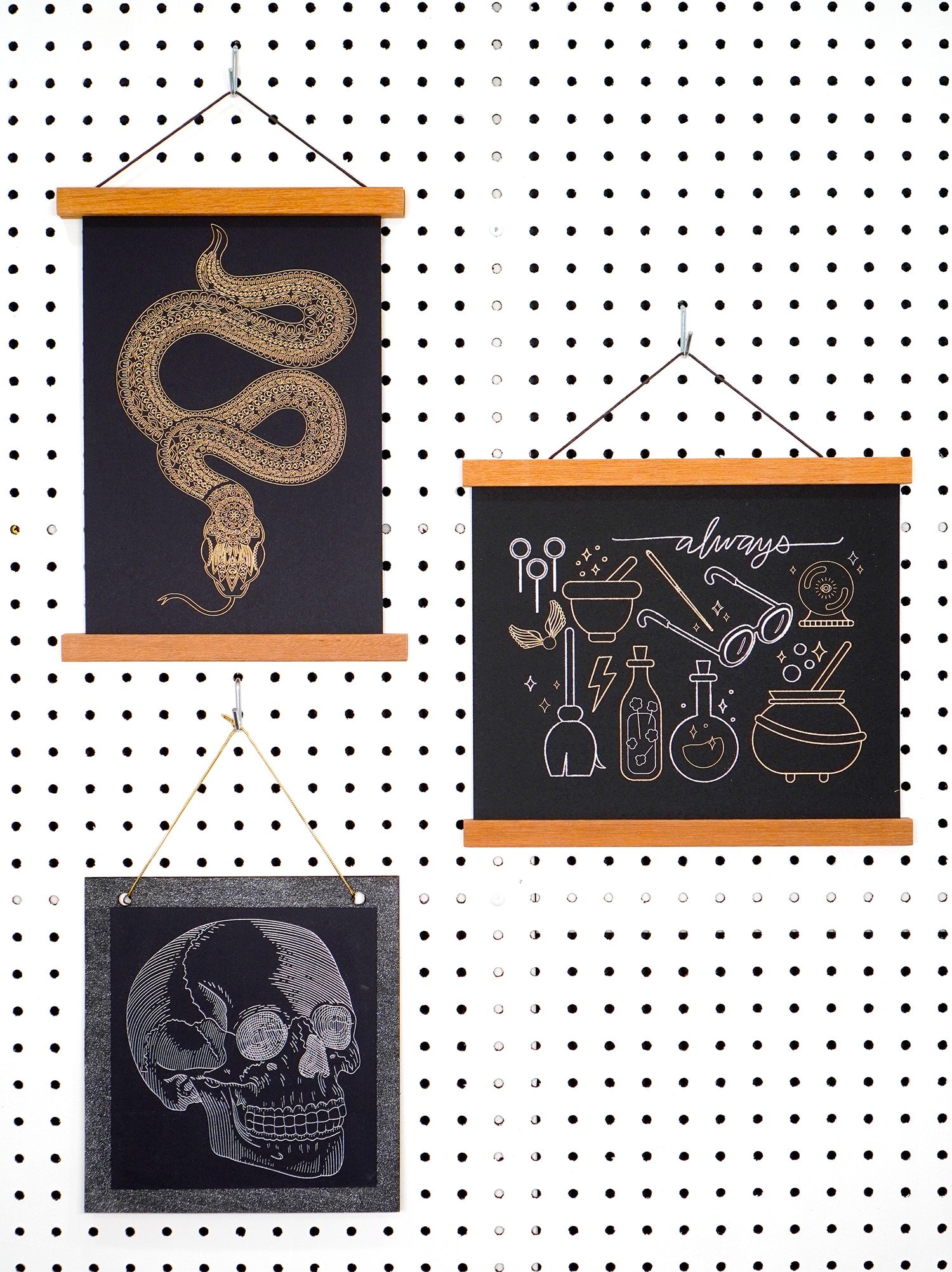 Gold and silver foil art prints (snake, skull, and wizardry) hanging on white pegboard