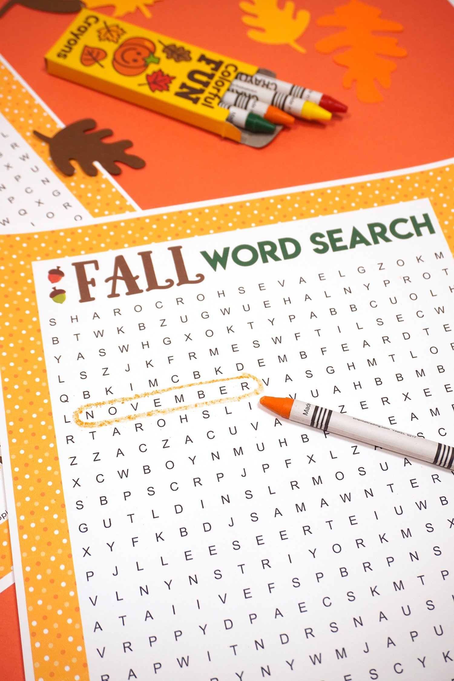 Fall Word Search Printable with "November" circled on dark orange background with orange crayon and paper leaves