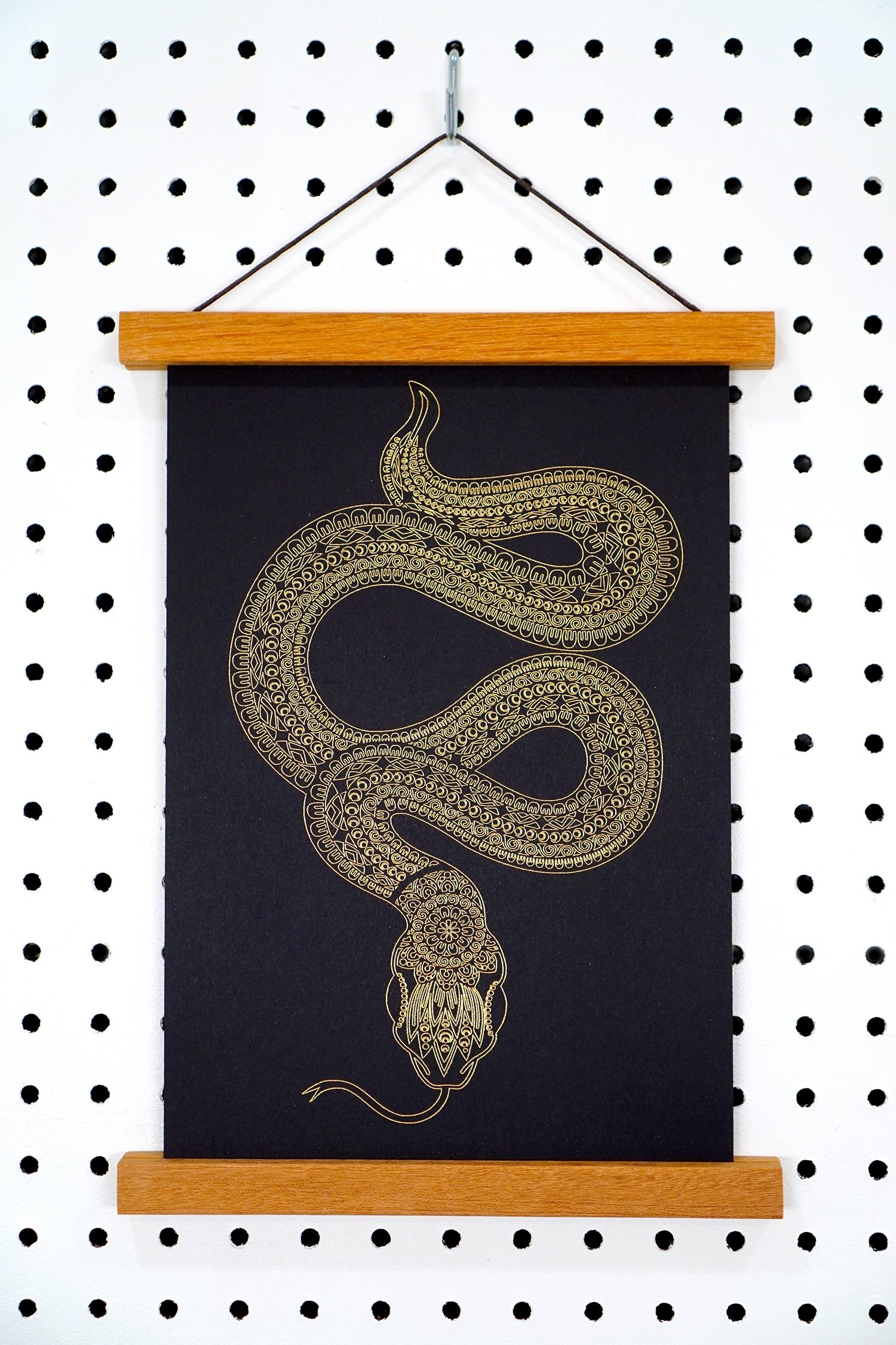 Gold foil art print of a snake with mandala design in wooden art hanger on pegboard