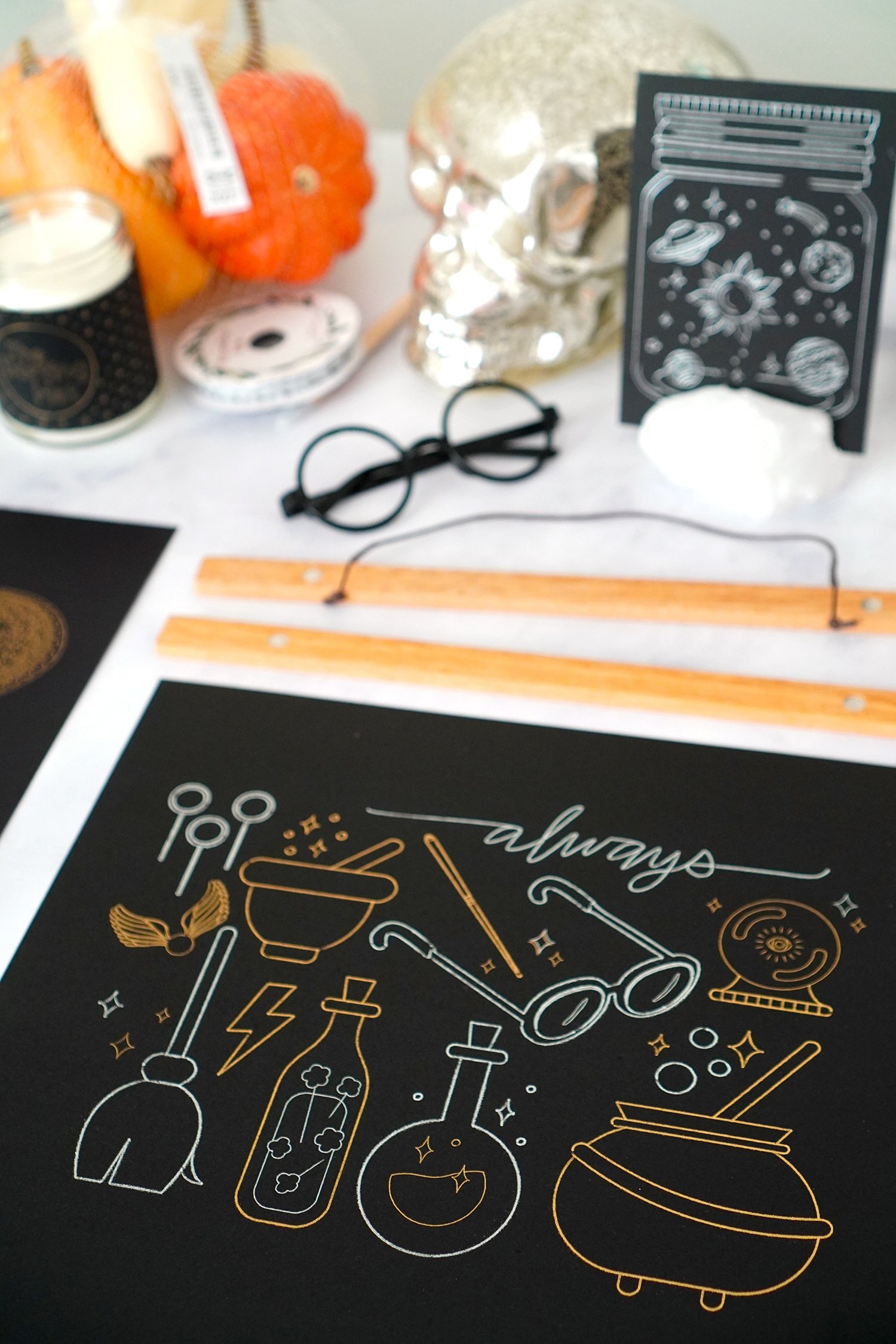Harry Potter inspired gold and silver foil artwork on table with picture hangers and Halloween props