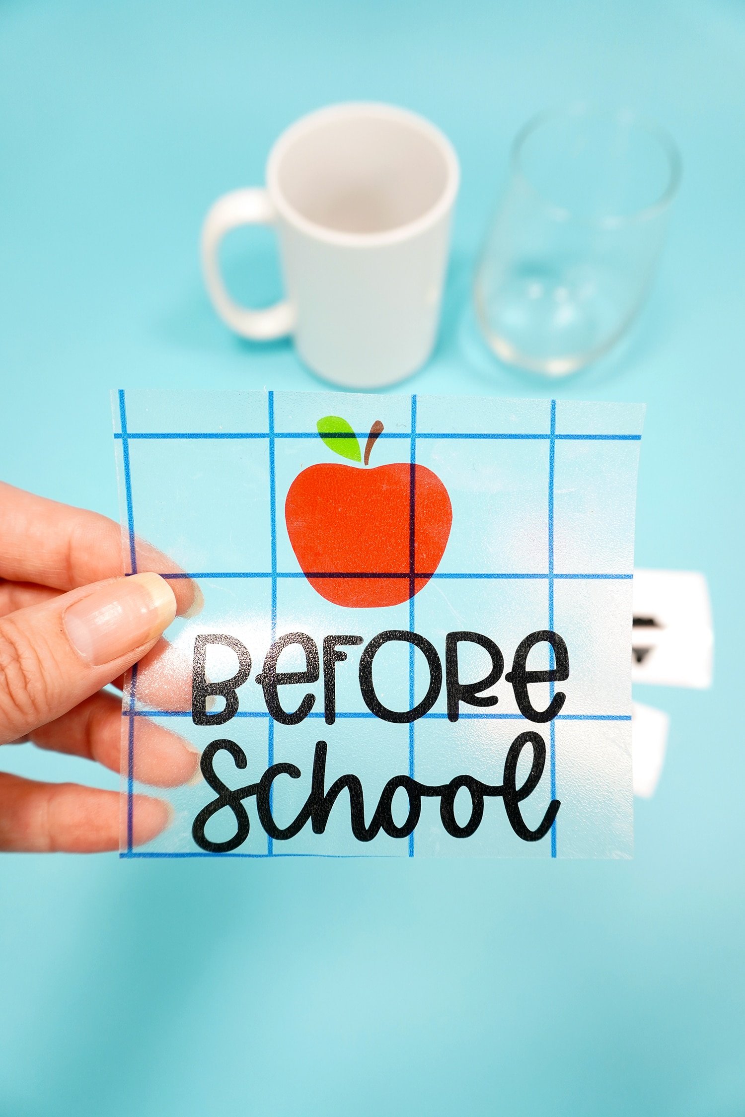 Hand holding apple and "before school" vinyl on transfer tape on blue backround