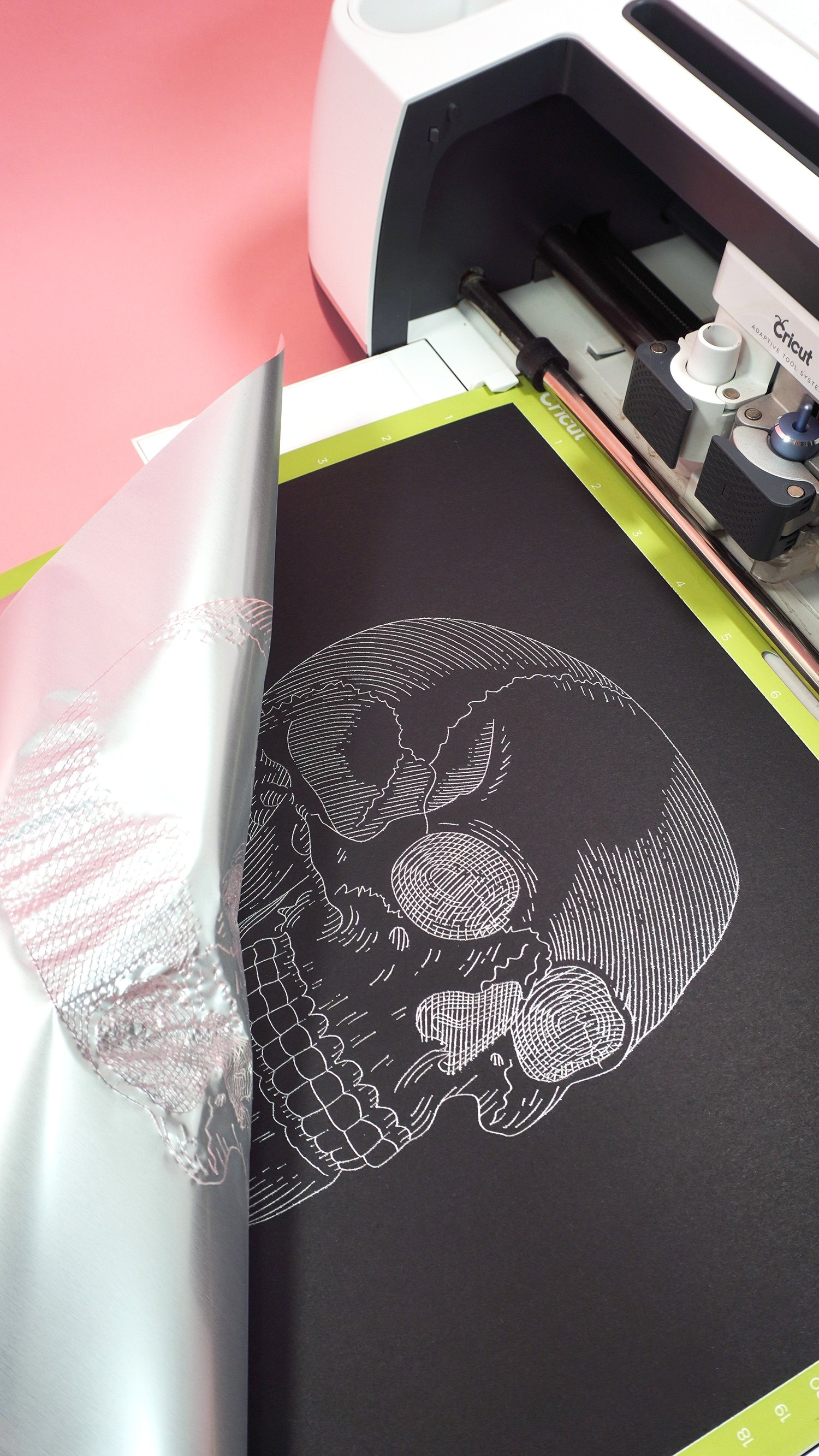Black kraft board on a Cricut mat in Maker machine with silver foil skull design