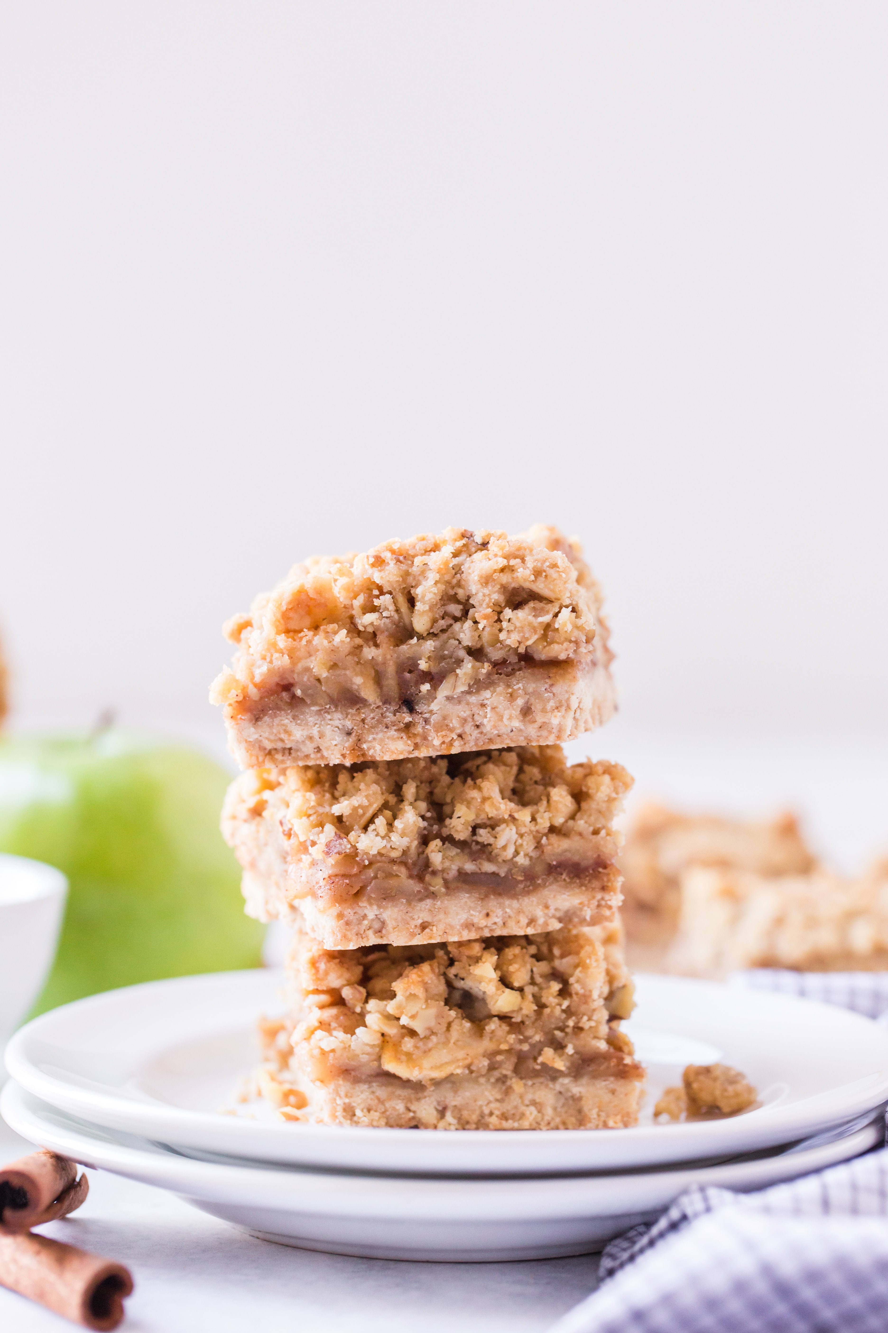 Three stacked apple pie bars with green apples and cinnamon sticks in background