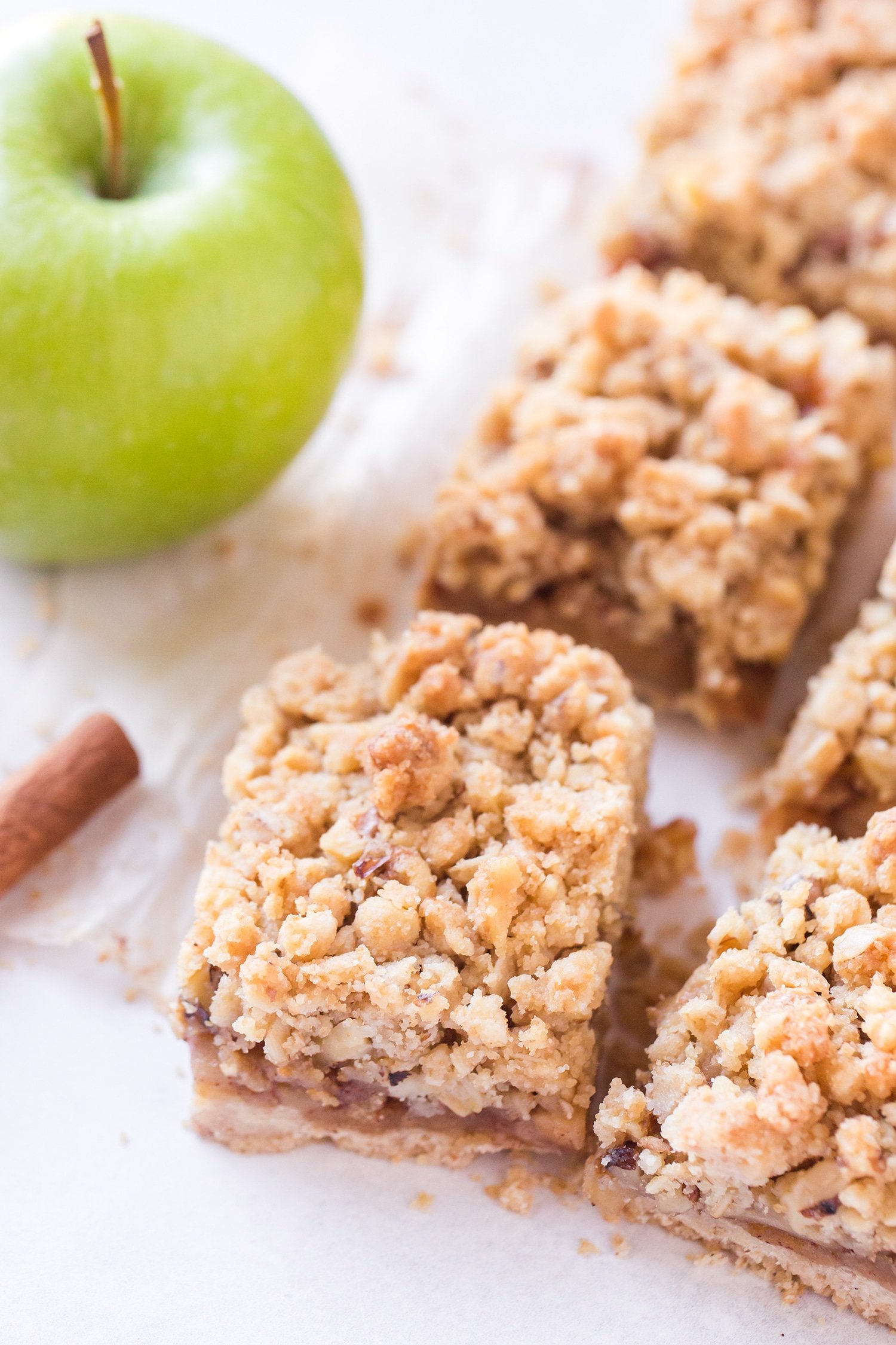 Sliced apple pie bars with green apples and cinnamon sticks in background