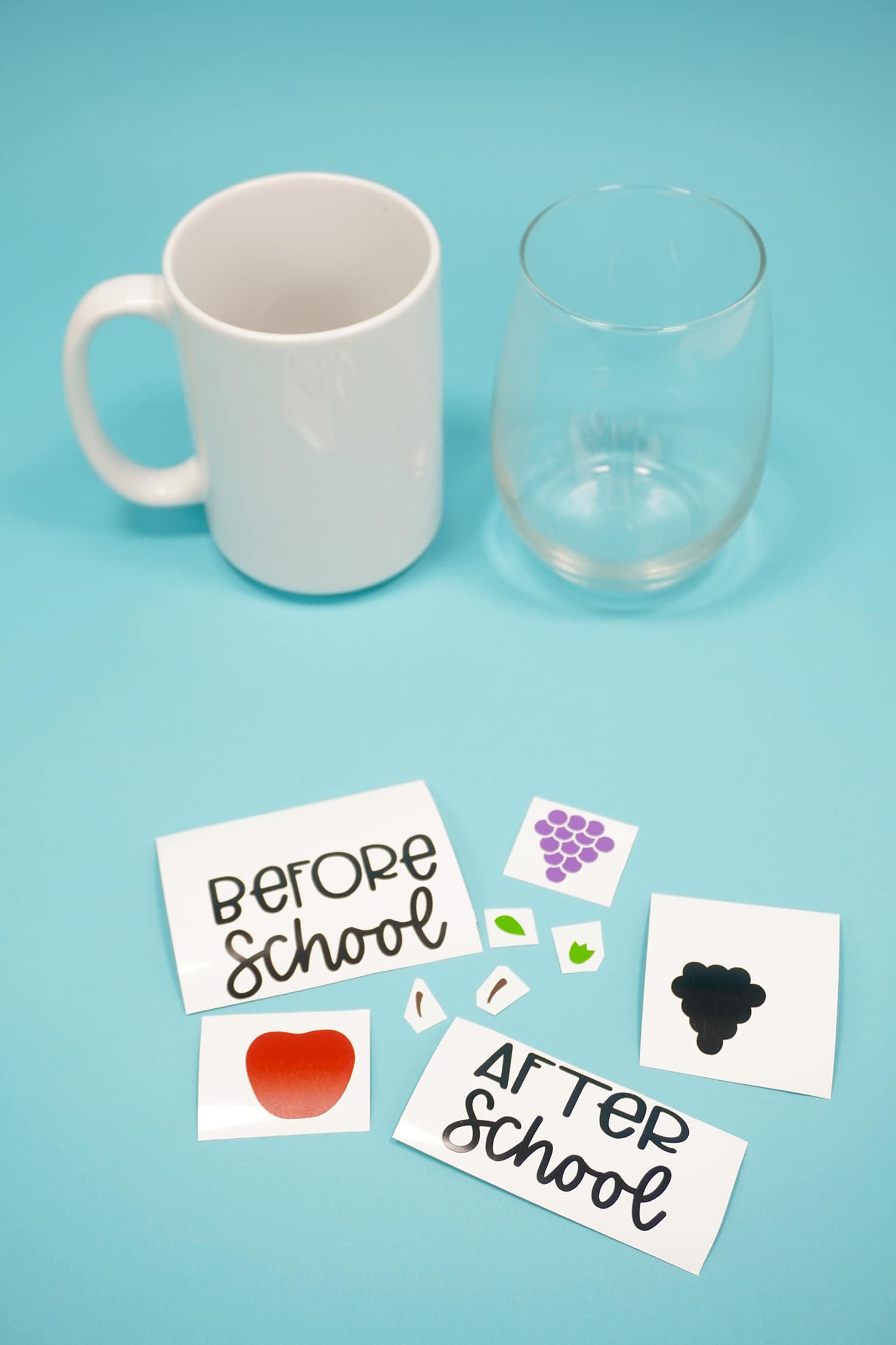 White mug and clear wine glass on blue background with assorted vinyl designs in foreground