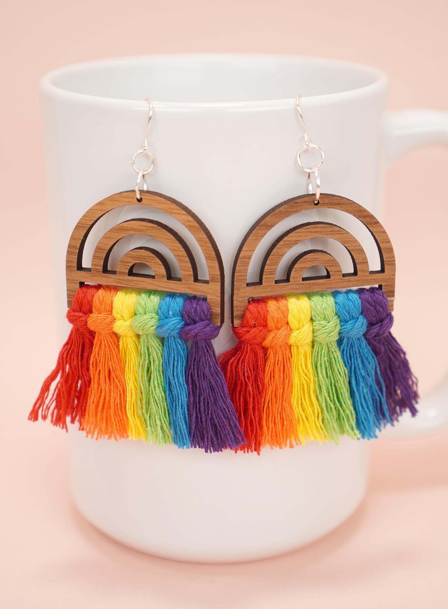 colorful wooden rainbow macrame earrings on white mug on peach background