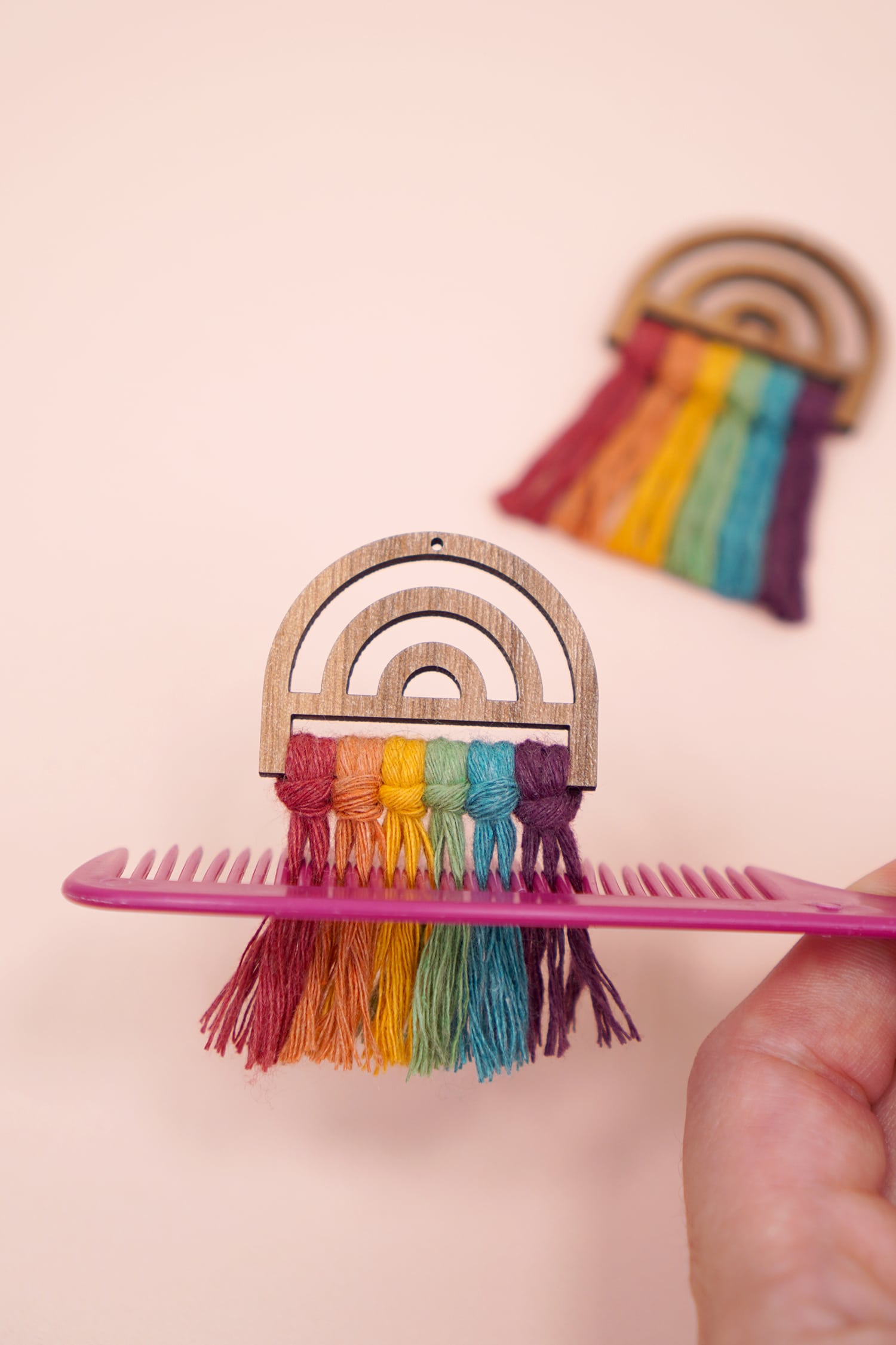 Combing a rainbow macrame earring with a pink comb on a peach background