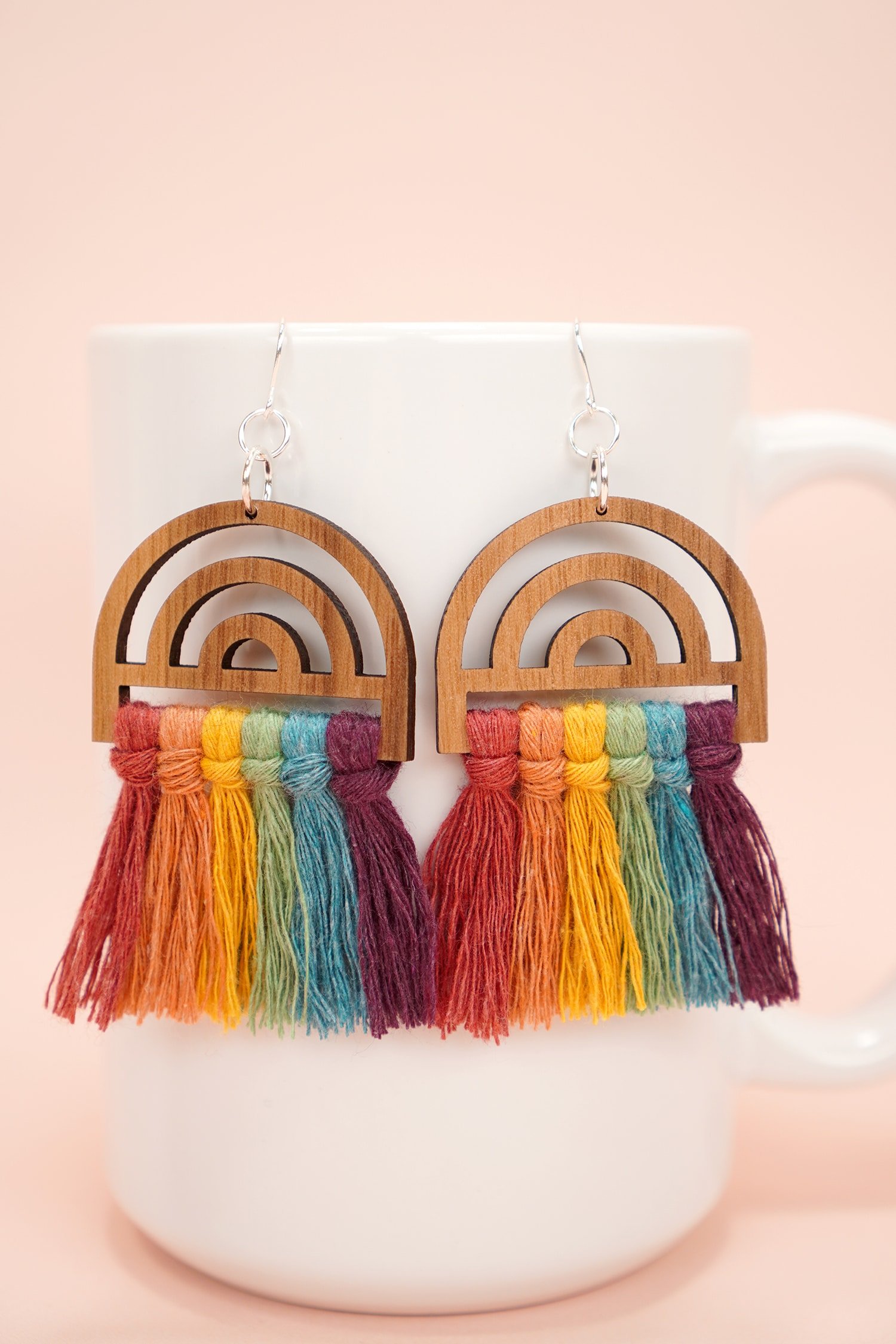 colorful wooden rainbow macrame earrings on white mug on peach background