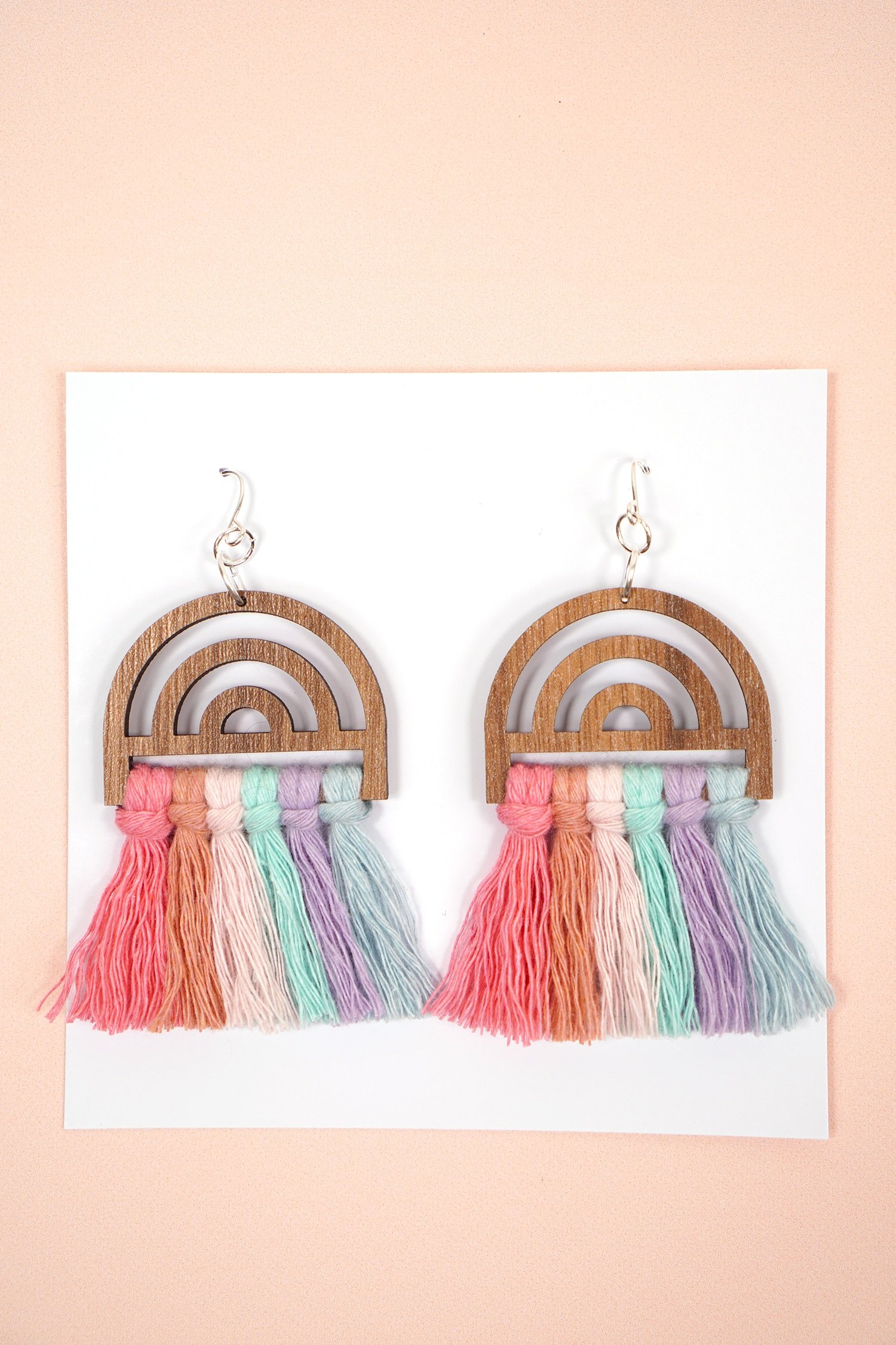 colorful wooden rainbow macrame earrings on white jewelry card on peach background