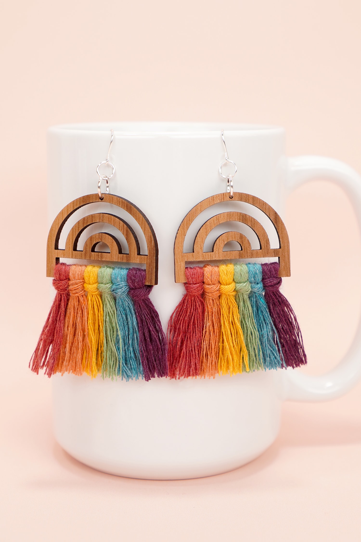 colorful wooden rainbow macrame earrings on white mug on peach background