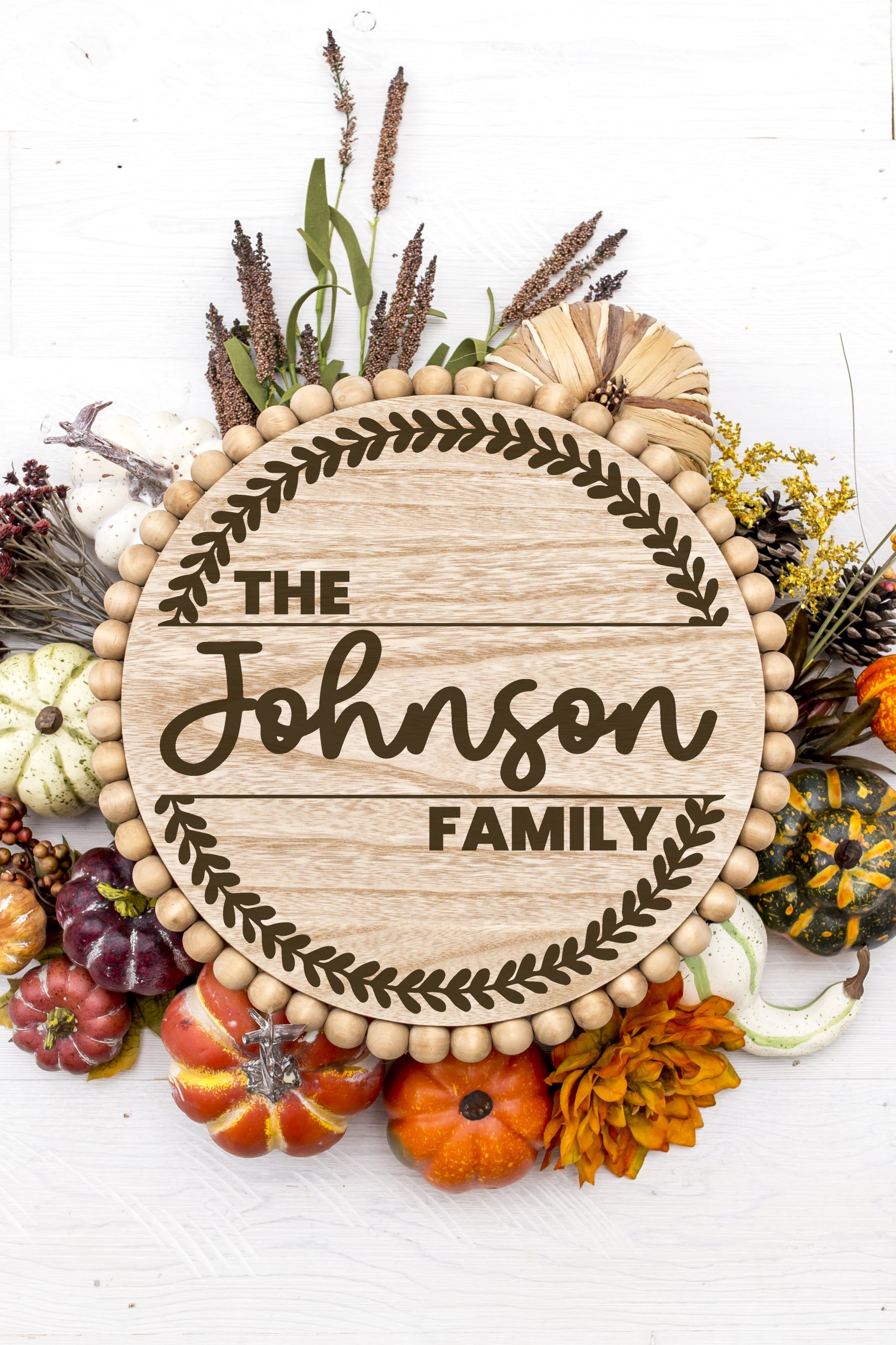 Round wood wreath with "The Johnson Family" design surrounded by fall pumpkins and foliage