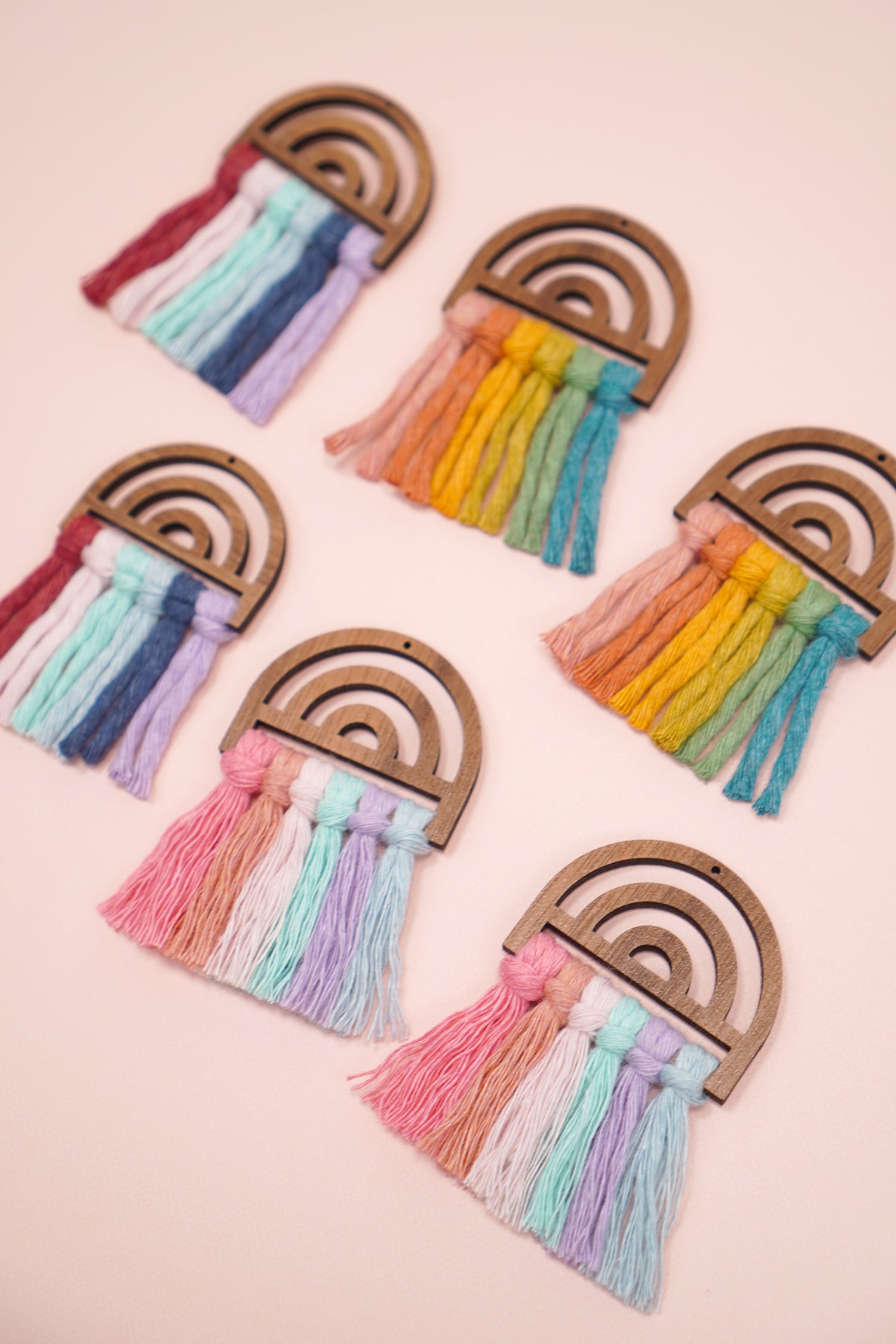 close up of different pairs of rainbow macrame earrings on peach background