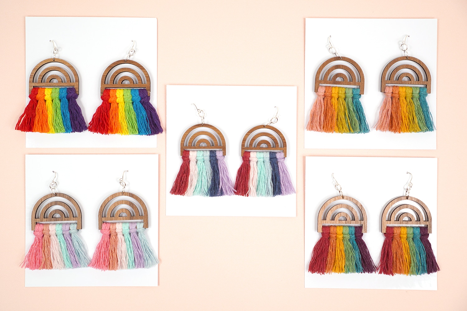 5 pairs of rainbow macrame earrings on white jewelry cards on peach background