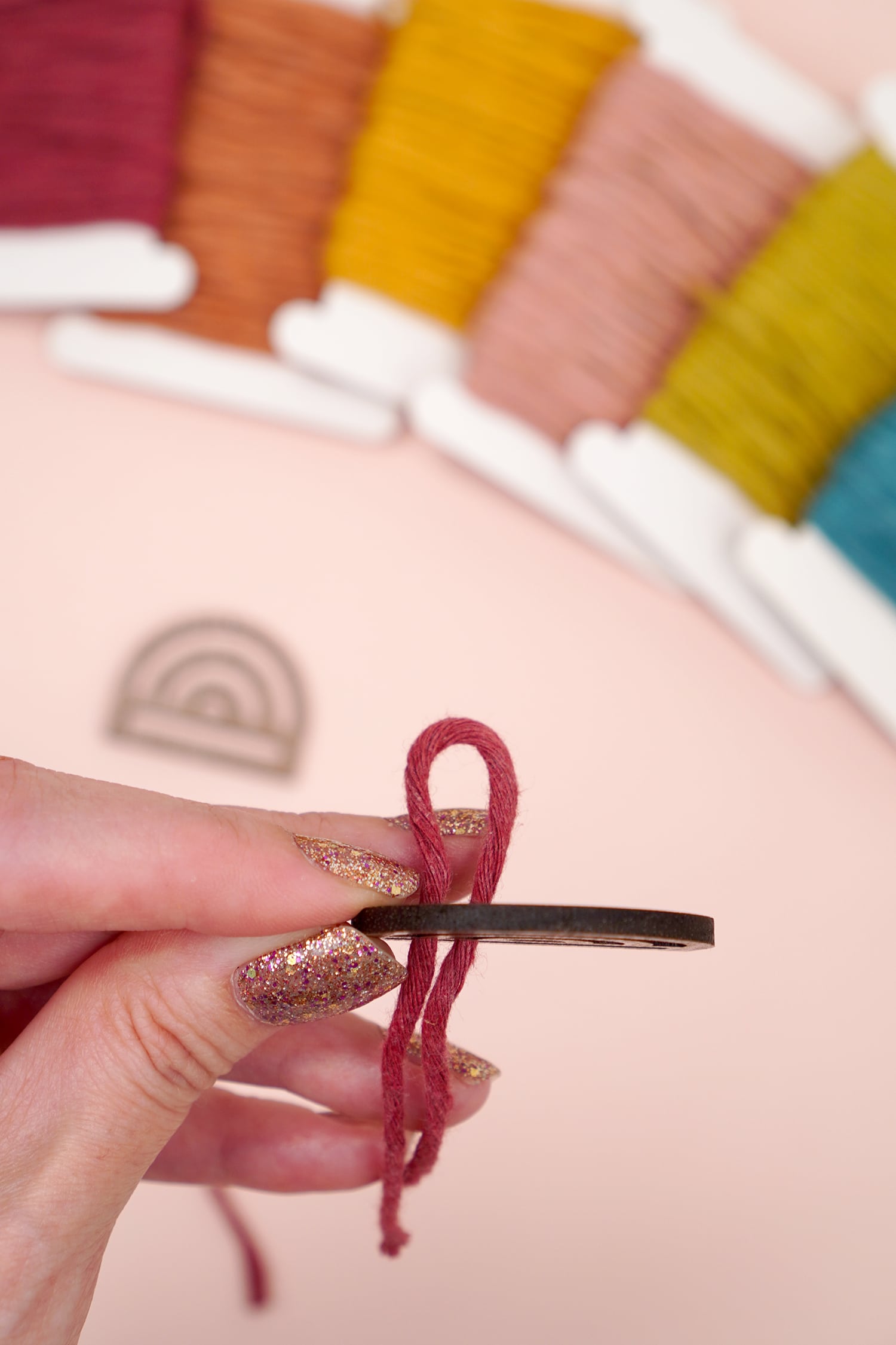 Threading macrame cord through rainbow wood finding on peach background with macramé cord