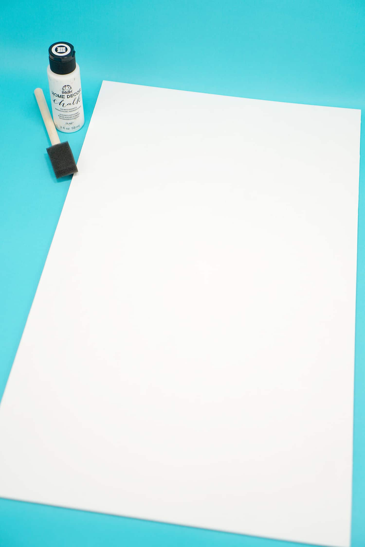 White painted board with white paint and paintbrush on aqua blue background