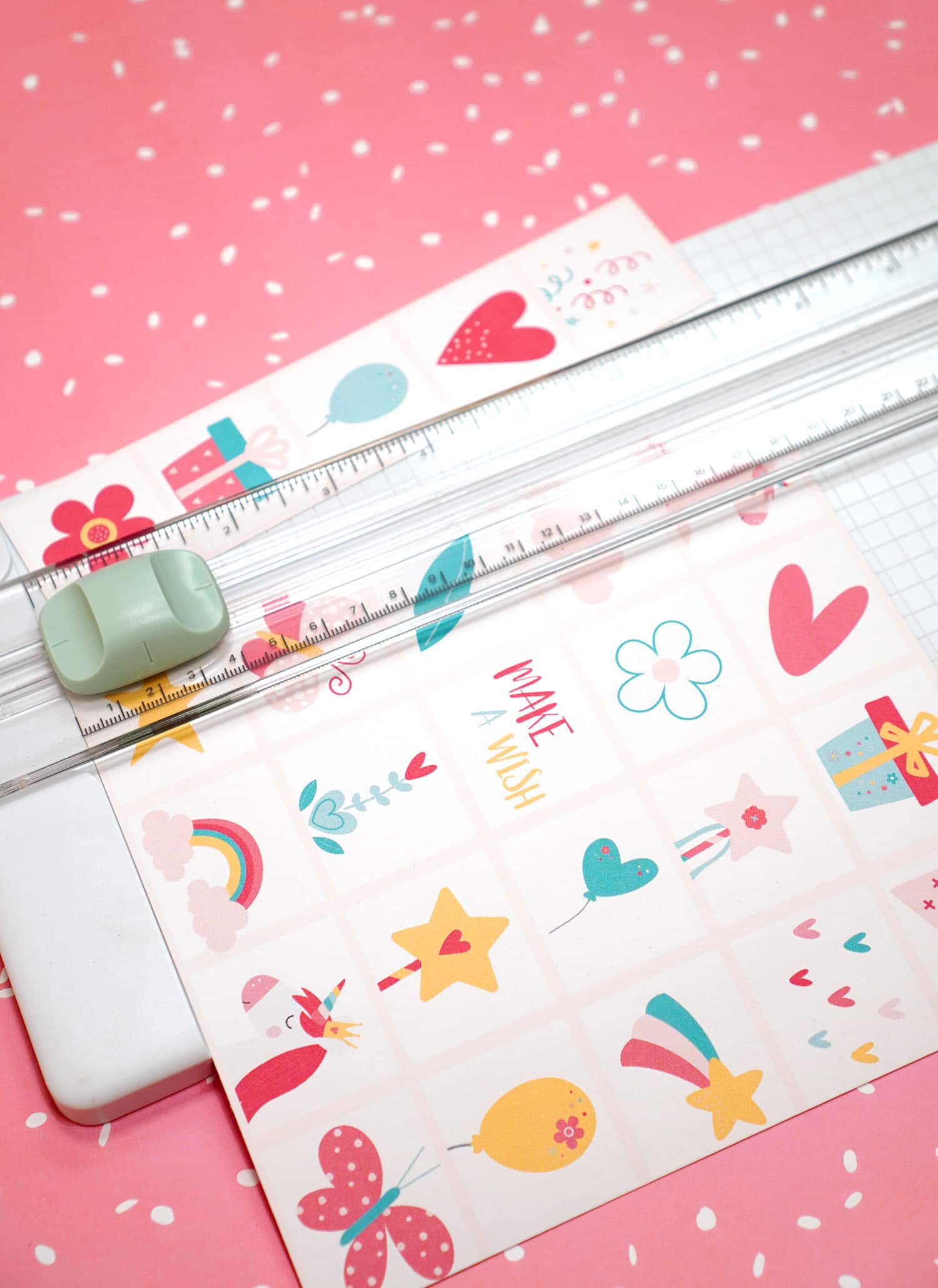 Paper trimmer cutting a sheet of Unicorn Bingo Game calling cards on a pink background
