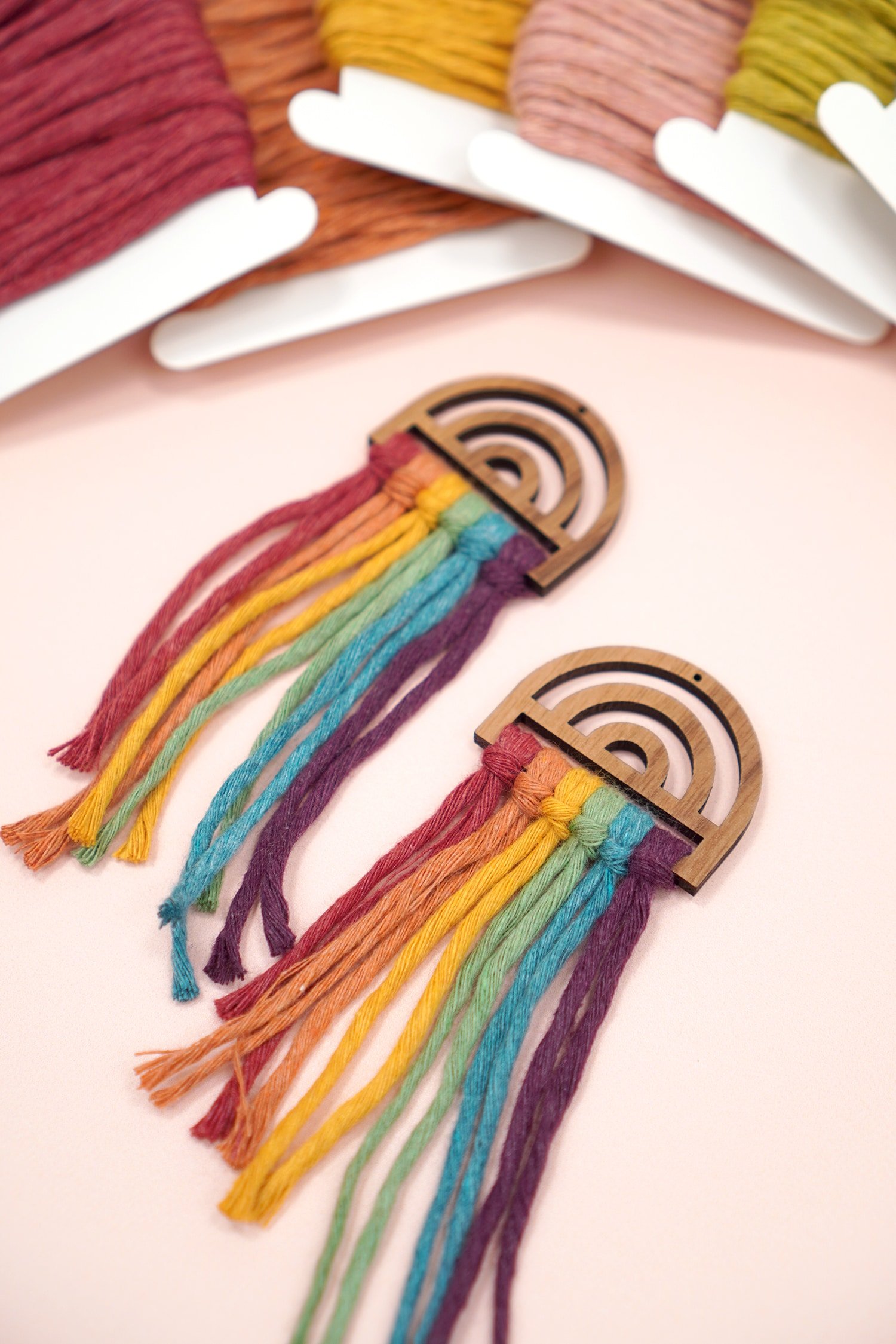 Untrimmed Rainbow Macrame Earrings on peach background with macrame cord
