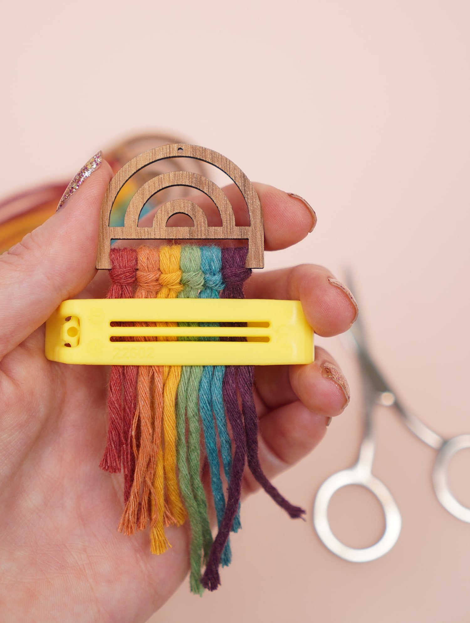 Hand holding rainbow macrame earring and Using a Bag Clip to Trim Macrame Earrings