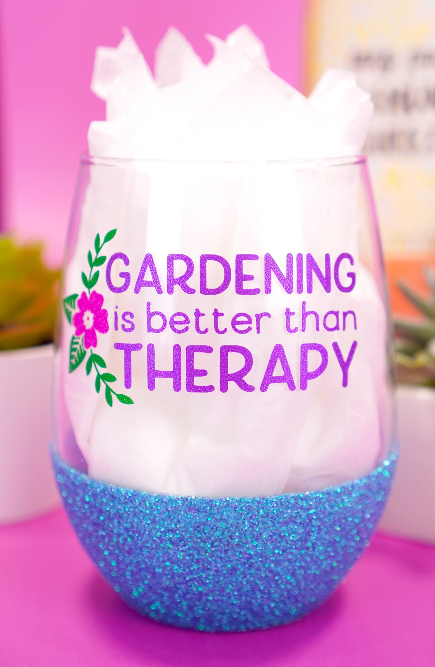 "Gardening is Better Than Therapy" stemless blue glitter wine glass on purple background with plants