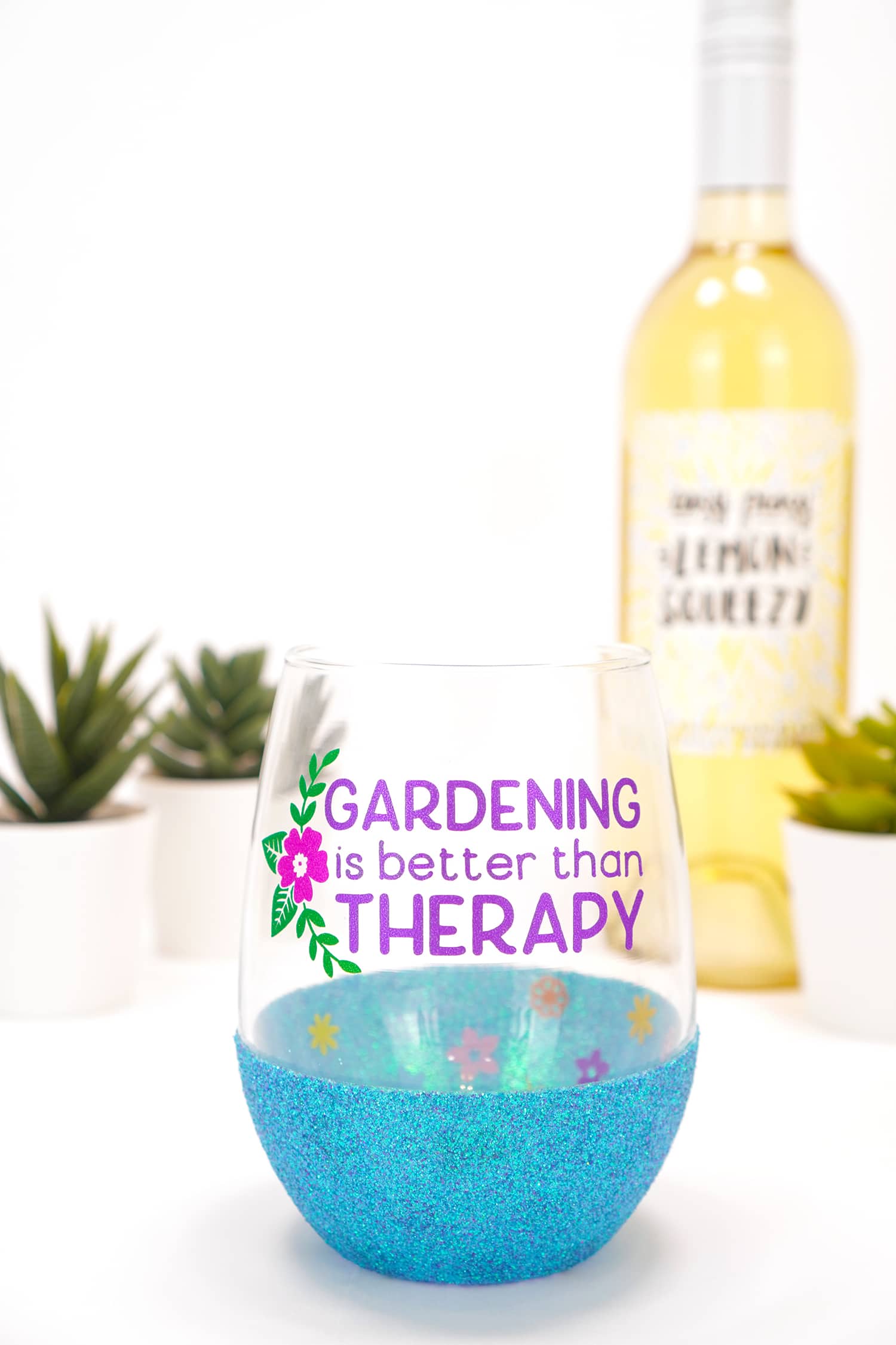"Gardening is Better Than Therapy" stemless blue glitter wine glass on white background with plants