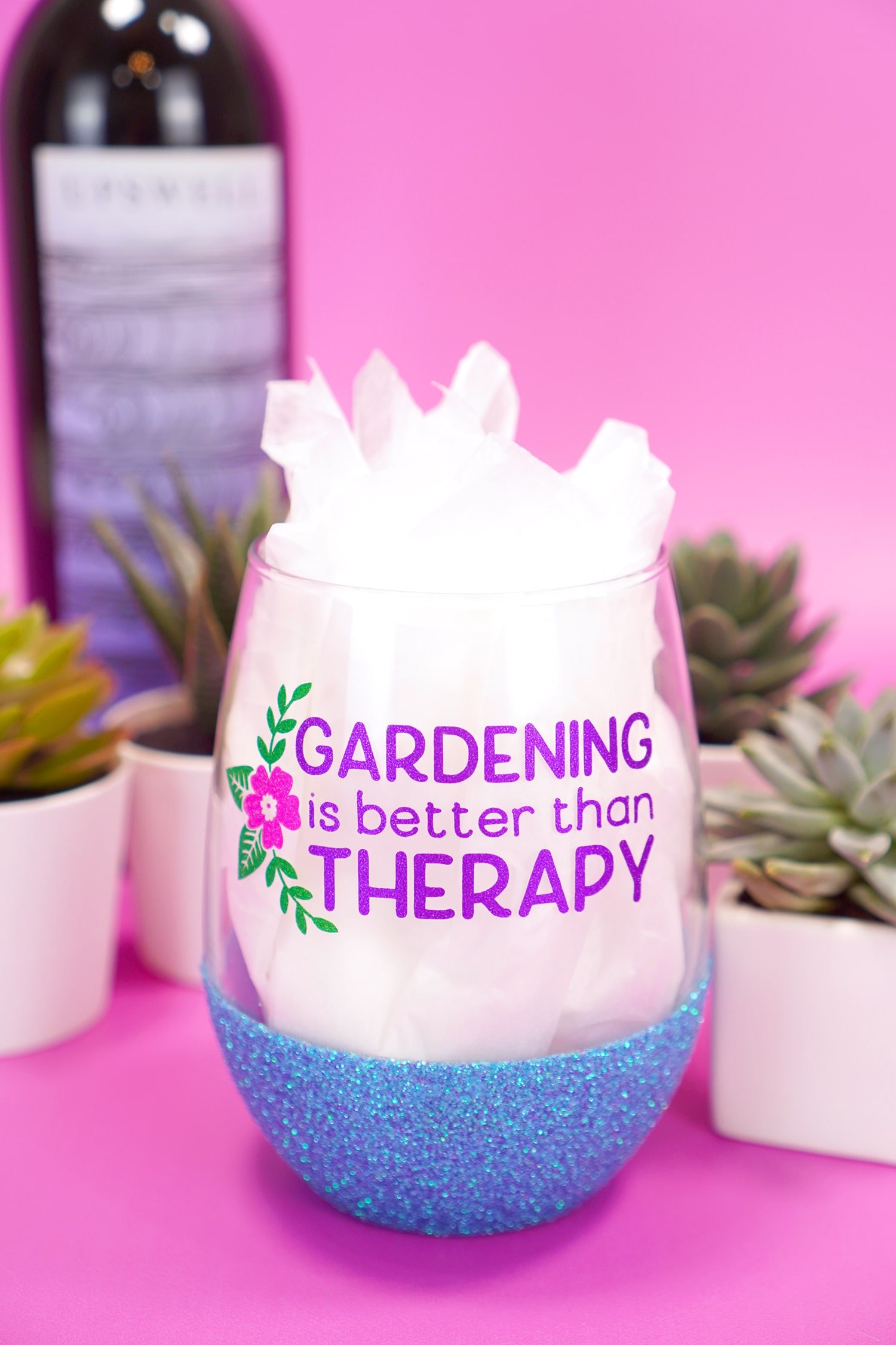 "Gardening is Better Than Therapy" stemless blue glitter wine glass on purple background with plants and wine bottle